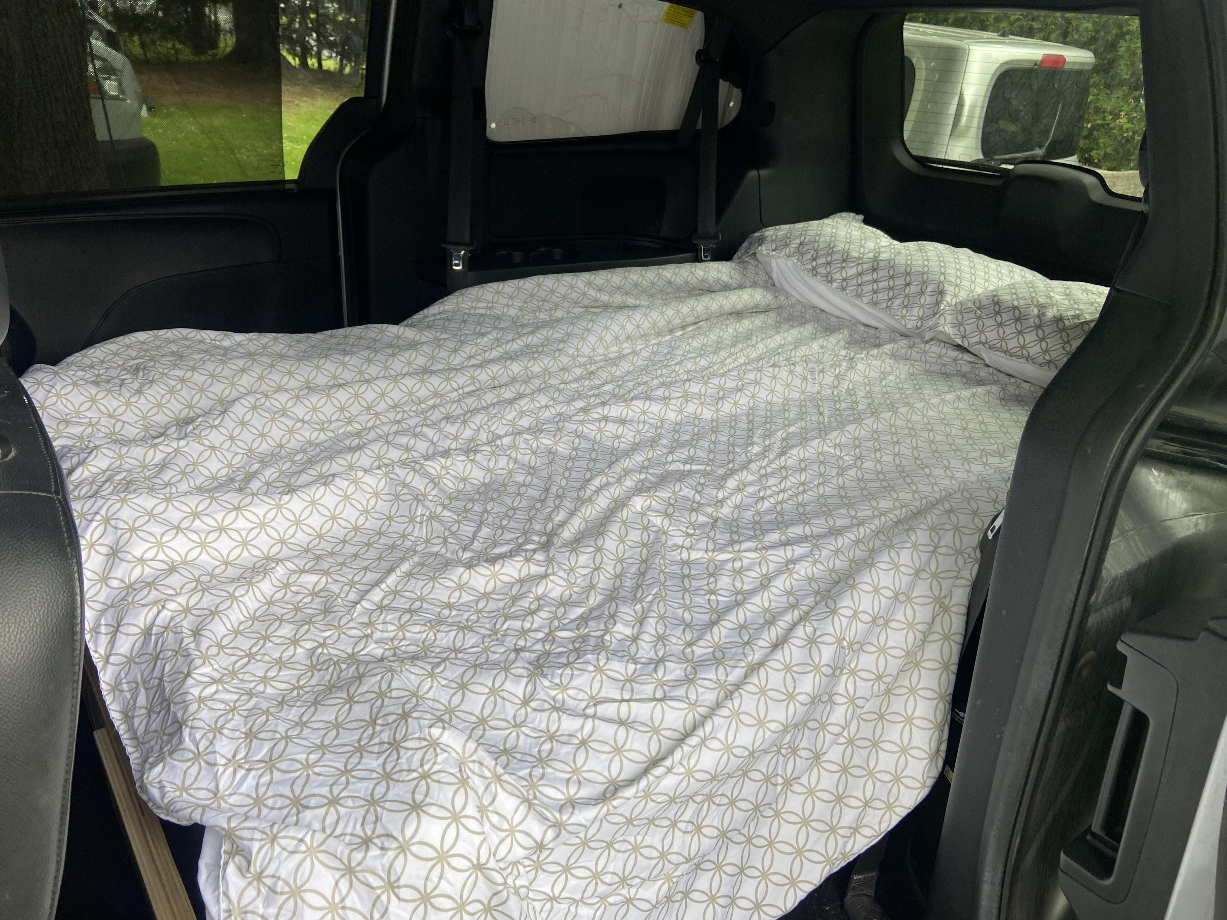 Inside an RV rental, a comfy bed with patterned sheets is ready for a van camping trip.. Dodge Caravan GT 2018