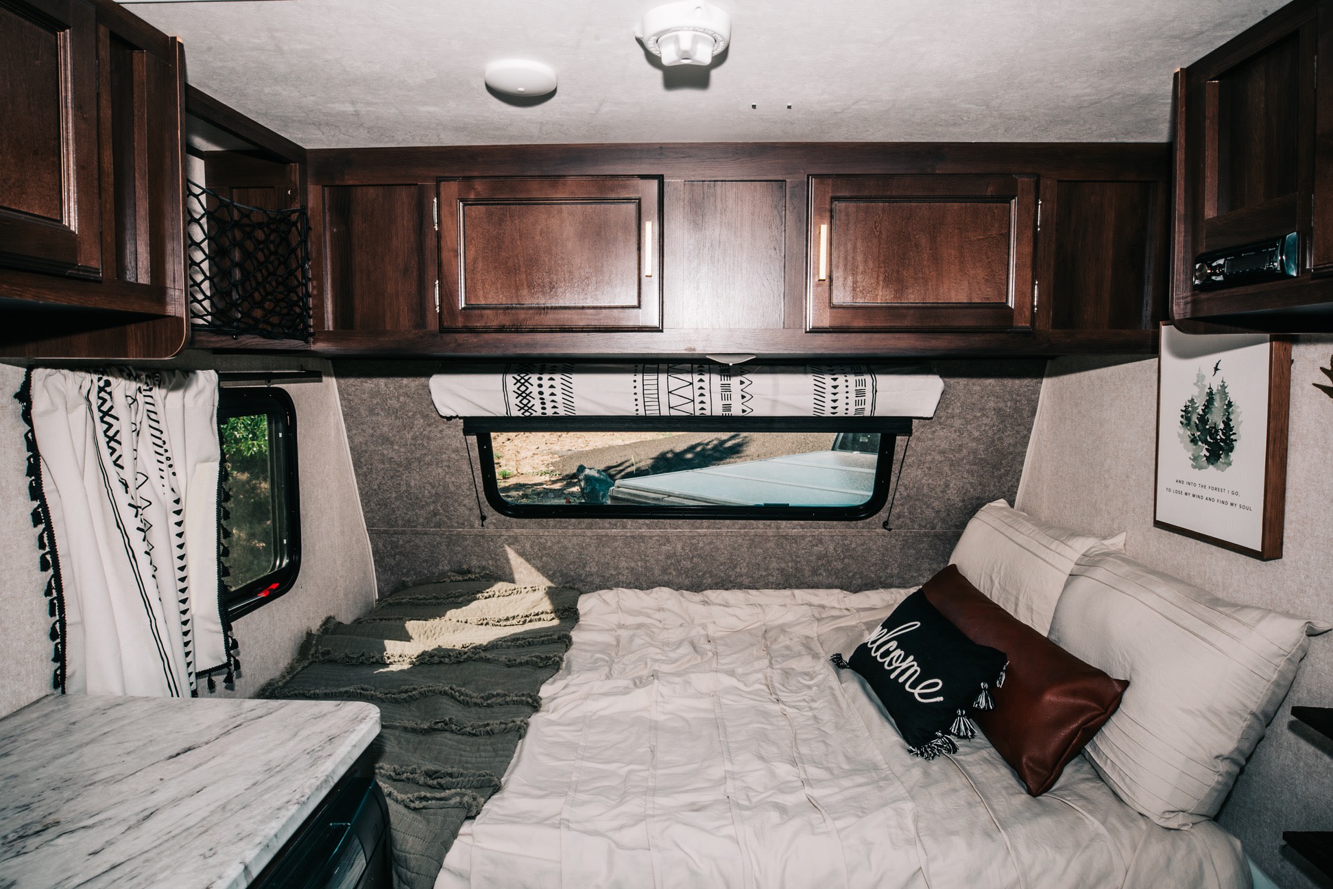 Cozy RV rental bedroom: dark wood cabinets, comfy bed, patterned window shade, and nature art create a perfect retreat.. Jayco Jay Flight SLX Baja Edition 2019