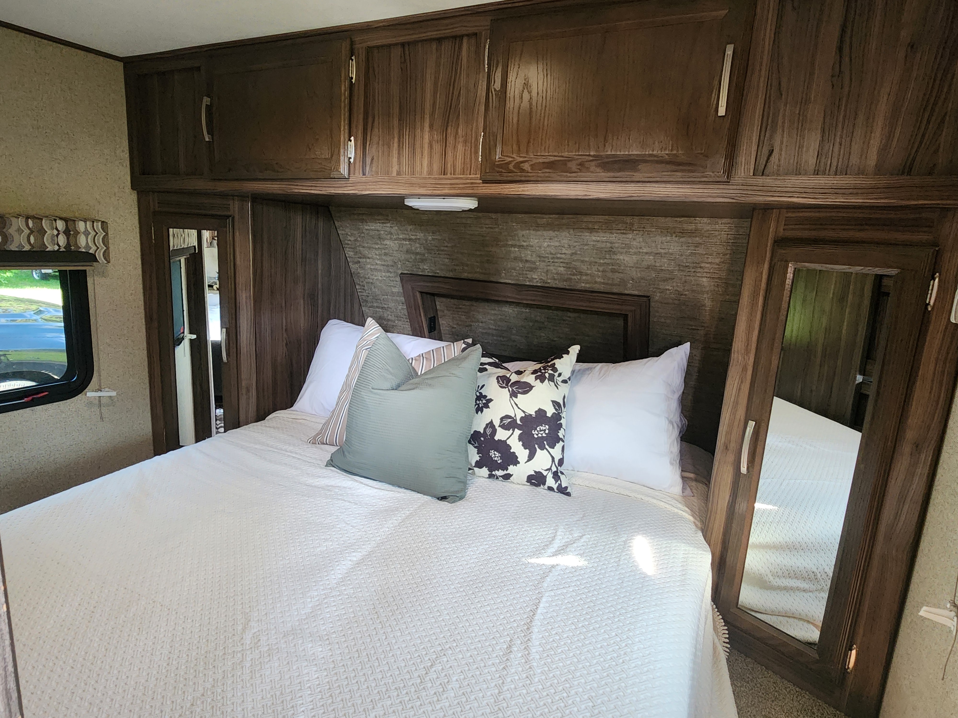 Cozy RV rental bedroom featuring a comfy bed with decorative pillows, overhead cabinets, and a mirrored wardrobe.. Coachmen Apex 2018