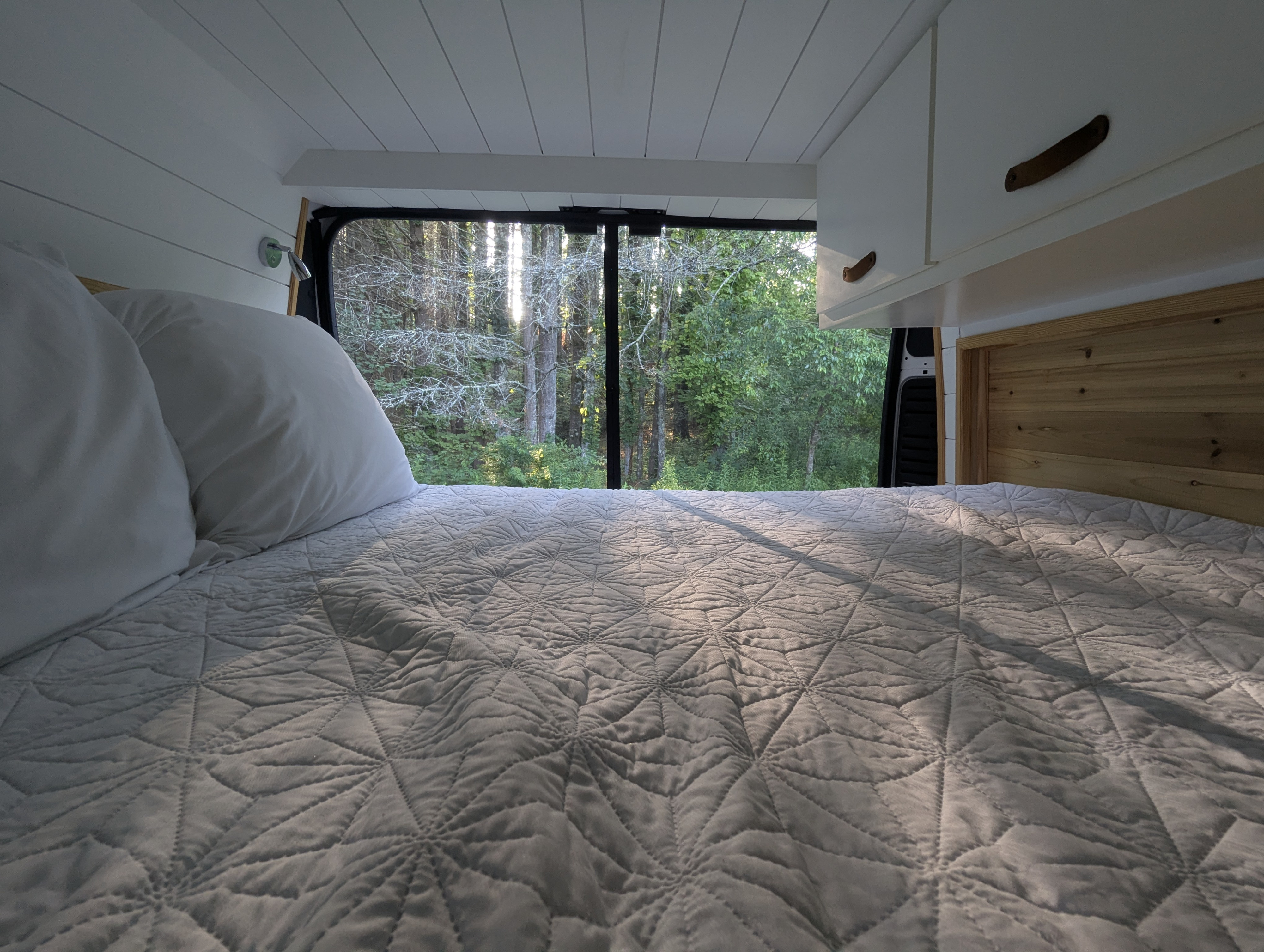 Cozy RV rental bedroom with quilted bed & forest view from large window. Perfect for nature escapes.. Dodge Ram Promaster 2500 2020