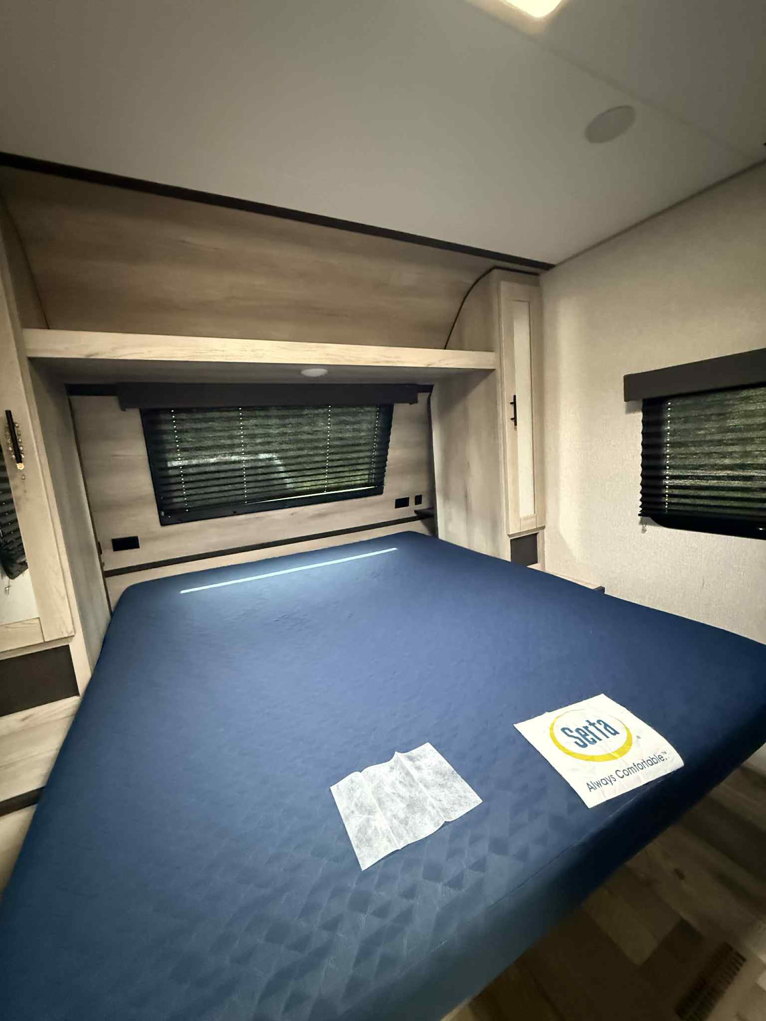 RV rental bedroom: A comfortable space with a blue Serta bed, overhead storage, and two windows with blinds.. KZ C261RB 2021