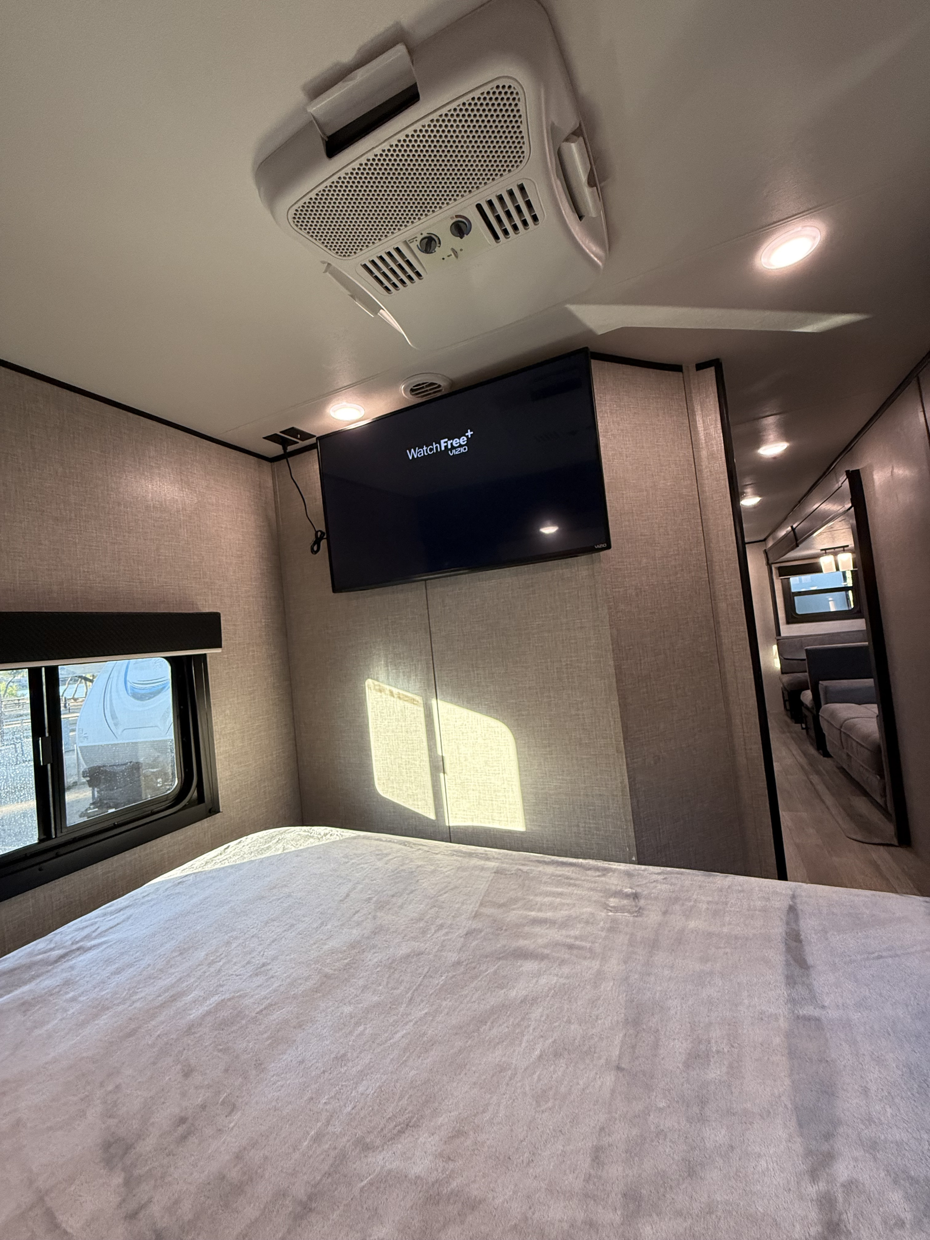 This RV rental's bedroom offers a cozy bed, wall-mounted TV, and ceiling AC unit. Bright interior for your RV journey.. Jayco Jay Flight 2022