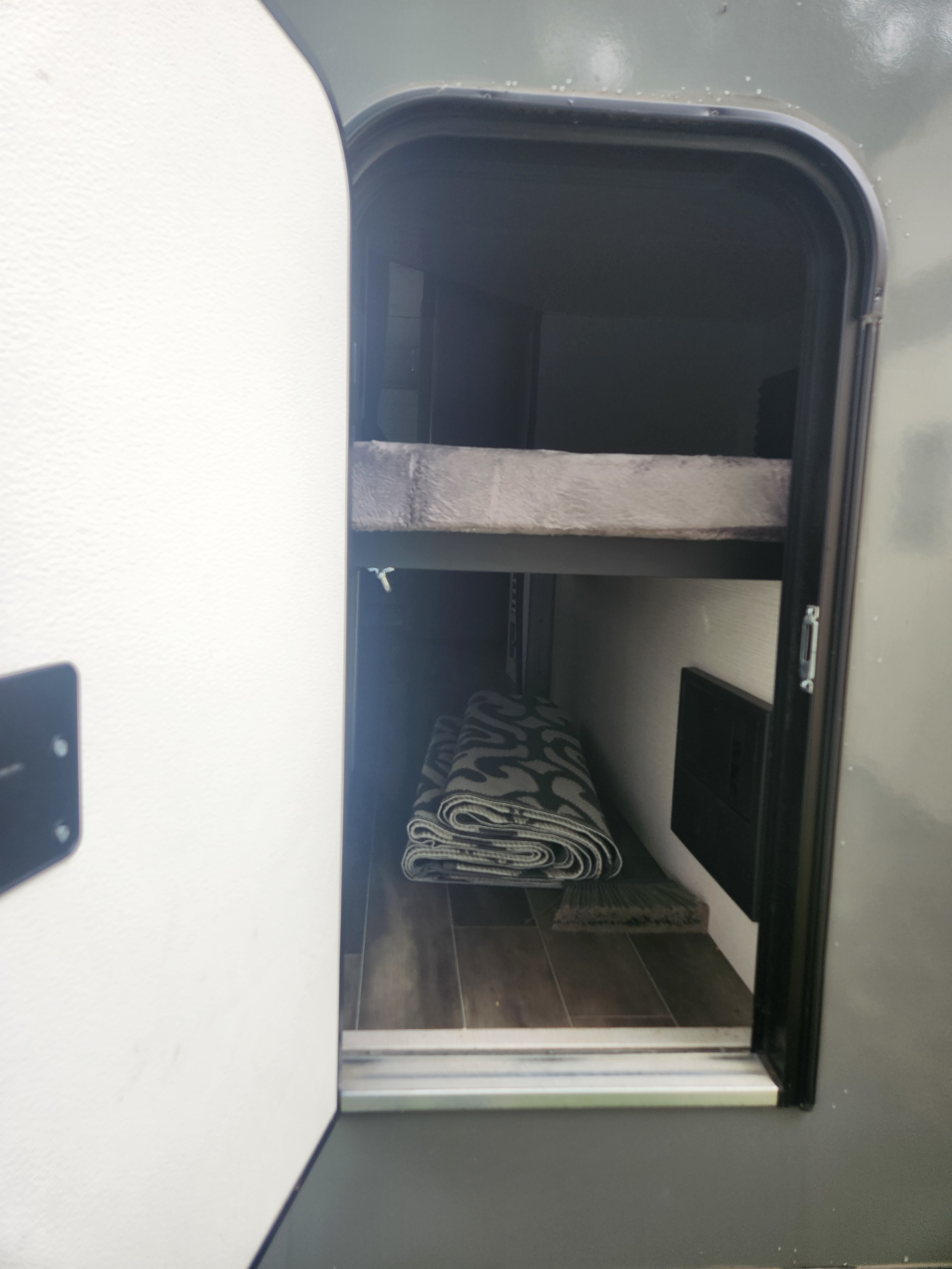 Compact RV rental interior showing a bunk bed, folded rug on wood flooring, and smart storage solutions.. Keystone RV Passport SL 2022