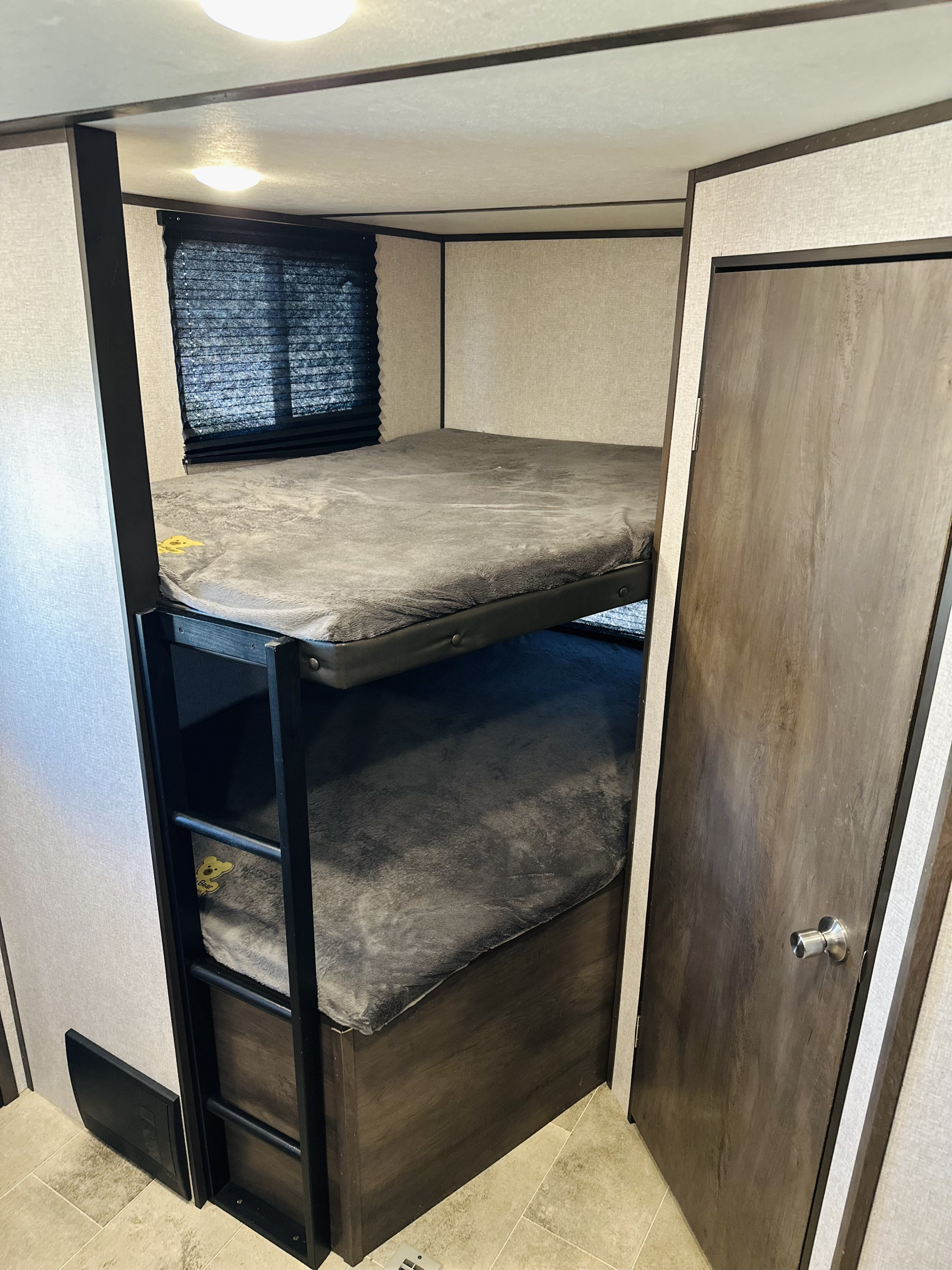 RV rental interior: Bunk beds with gray mattresses, a ladder, window, and adjacent door for compact sleeping.. Dutchmen Coleman Lantern 2021