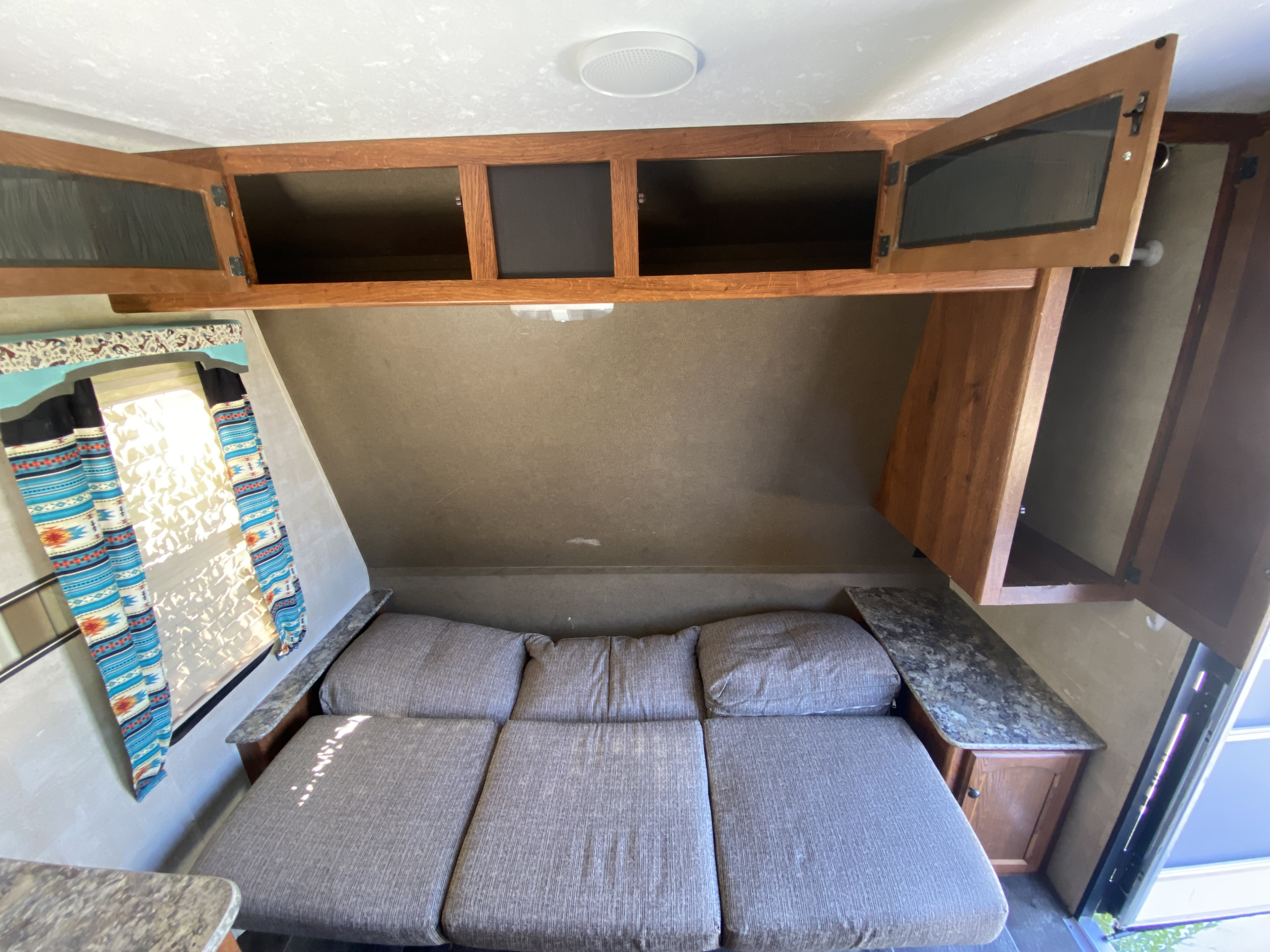RV rental interior featuring a convertible bed/sofa, ample overhead storage cabinets, and a bright window with unique curtains.. Keystone RV Hideout 2015