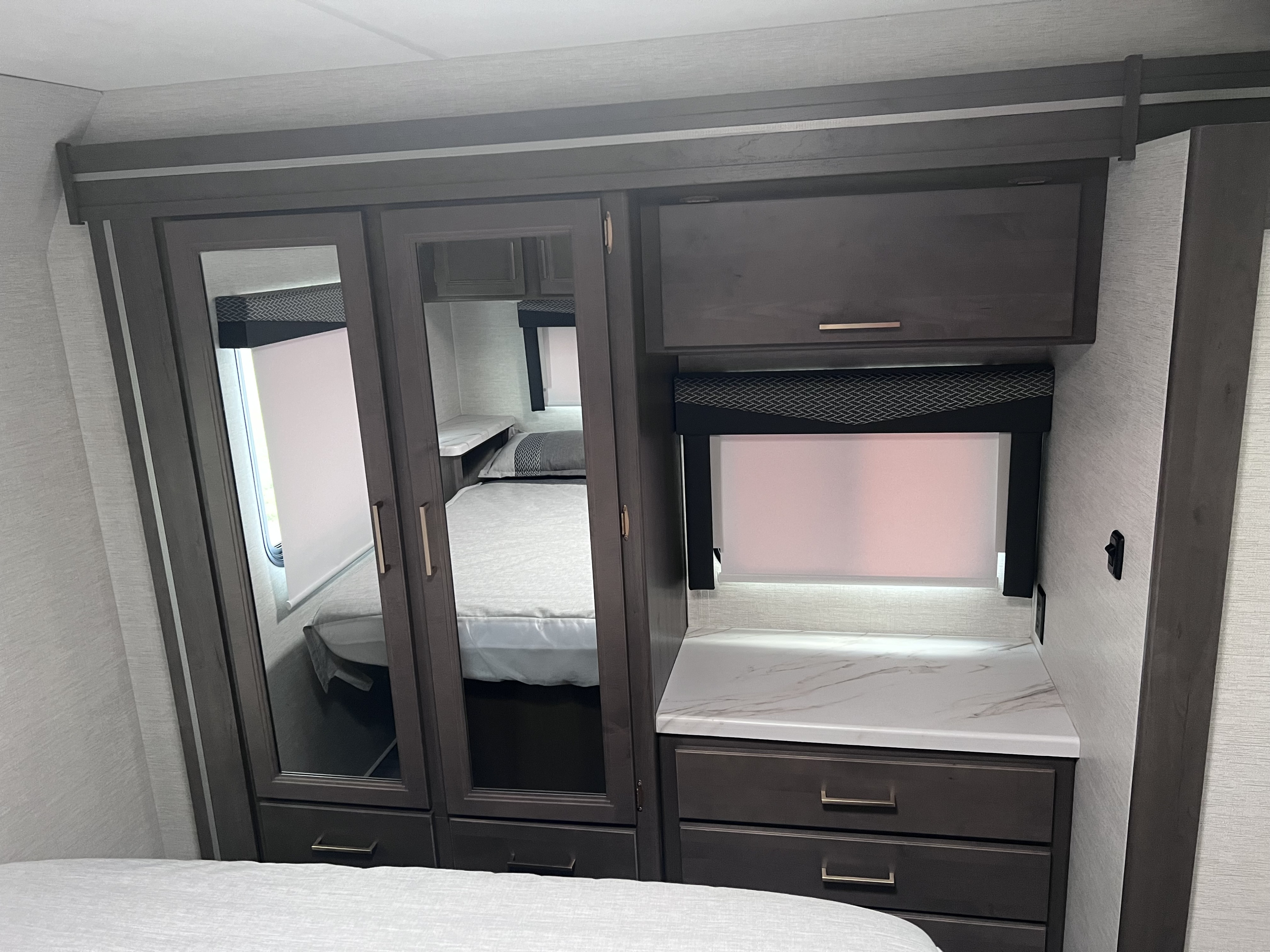 Explore this RV rental bedroom featuring a built-in mirrored closet, countertop, and window with a shade.. Thor Four Winds 2024