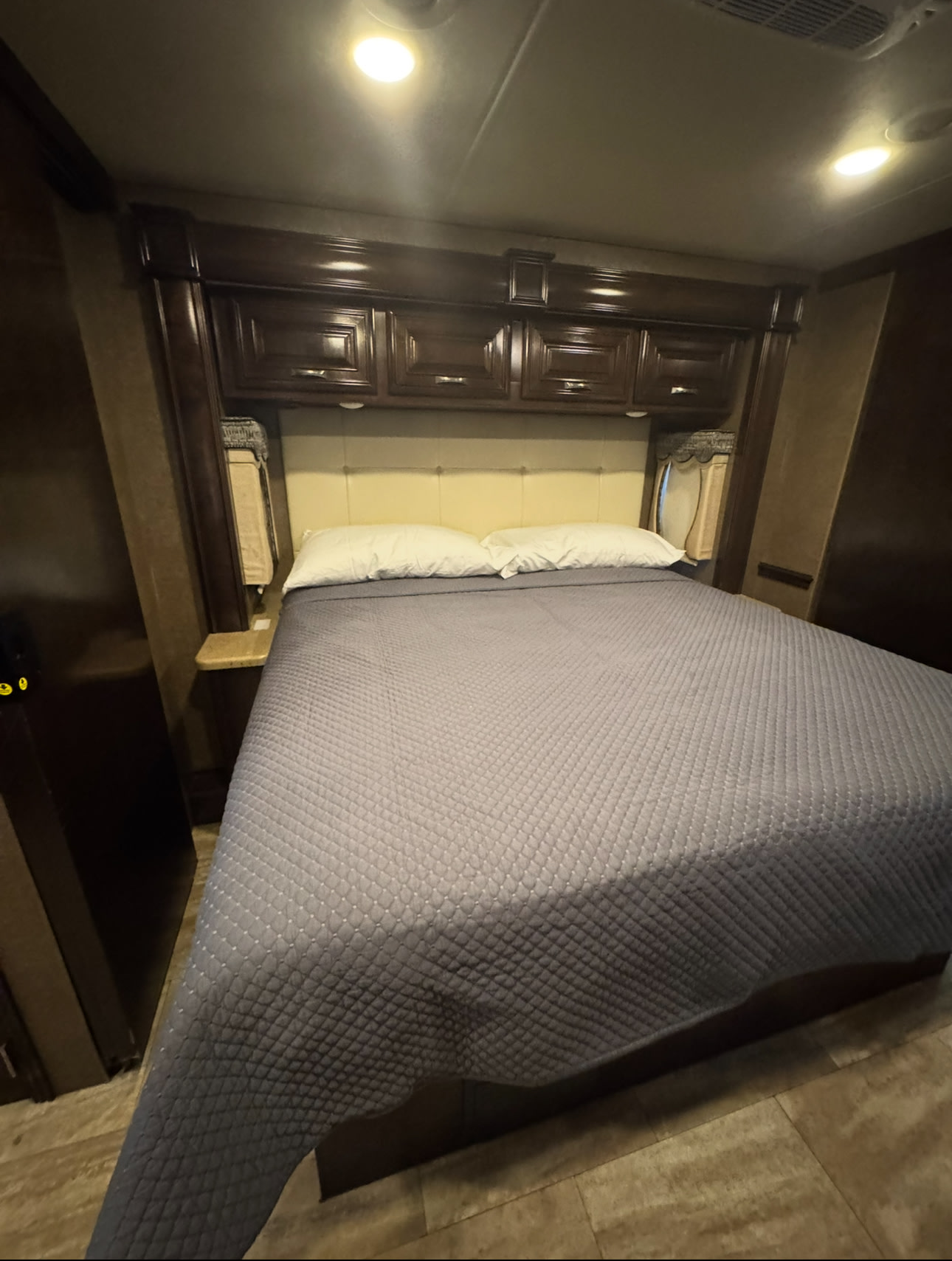 Spacious RV rental bedroom with dark wood overhead cabinets, a queen bed, light headboard, and side nightstands.. Thor Challenger 2017