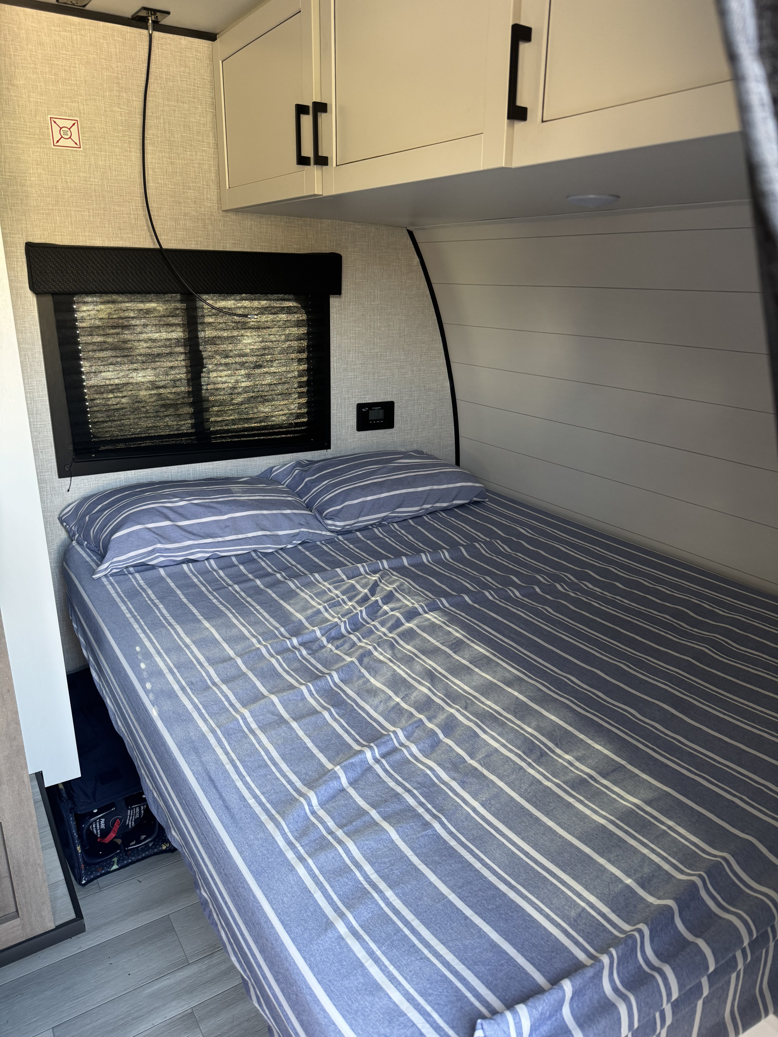 RV rental bedroom interior: a neatly made bed with blue & white striped bedding, overhead cabinets, and a window with blinds.. 58TBM0AK1S75M3067 180bhs 2025