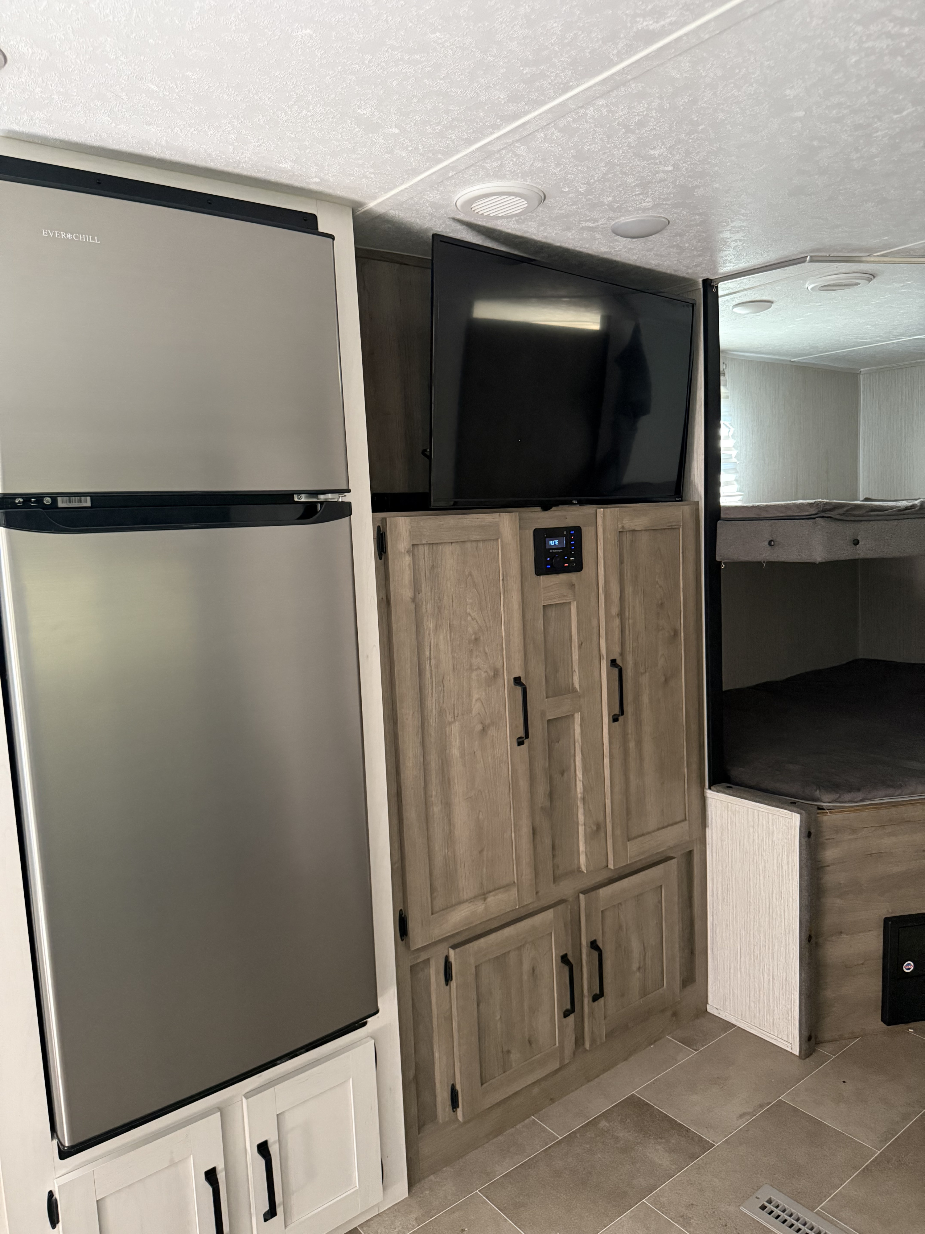 RV rental interior featuring a large stainless steel refrigerator, TV, wood cabinetry, and convenient bunk beds.. Forest River Palomino Puma XLE Lite 2021
