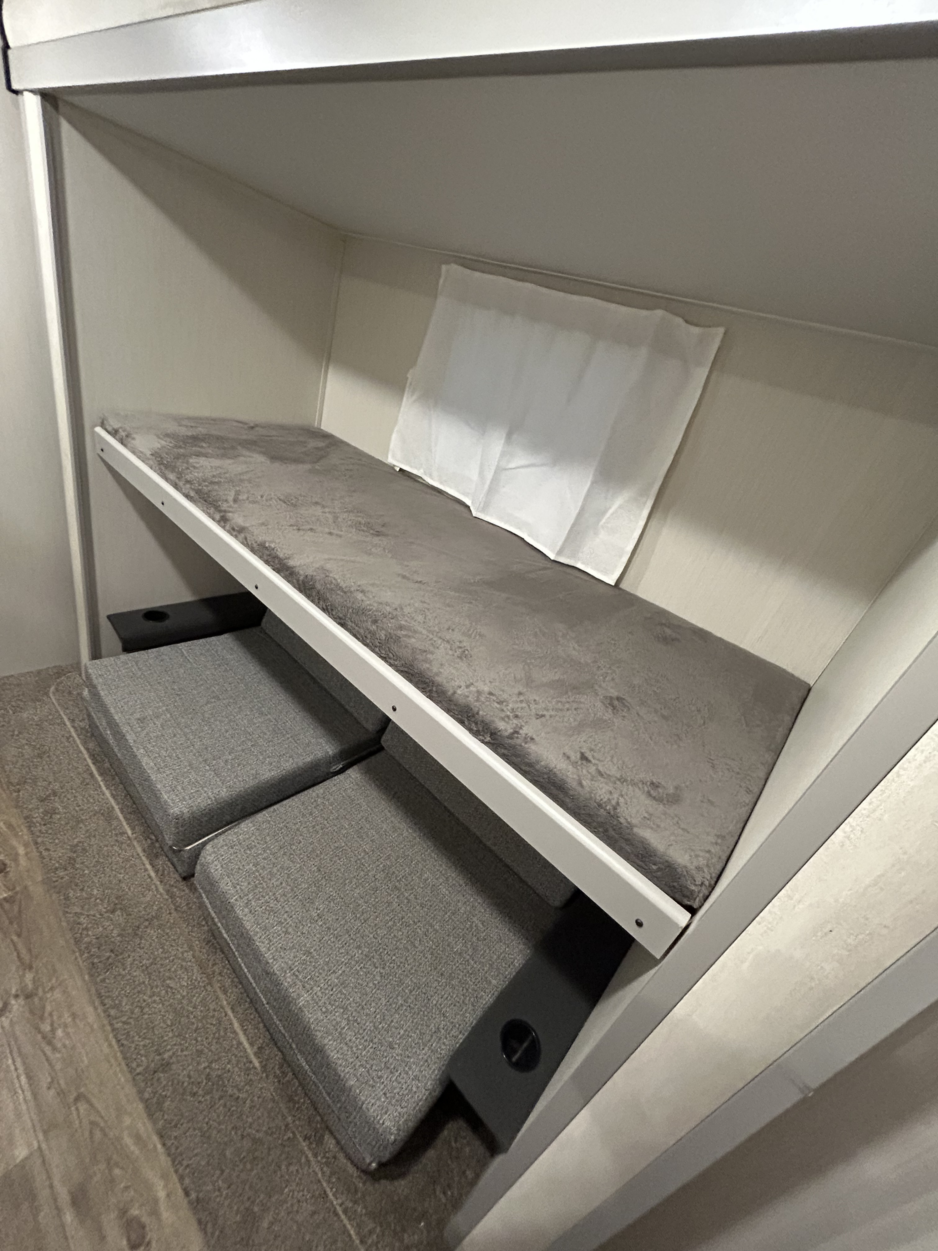 Cozy RV rental bunk bed with soft grey mattress, convertible lower seating, and convenient cup holder.. Forest River Vibe 2022