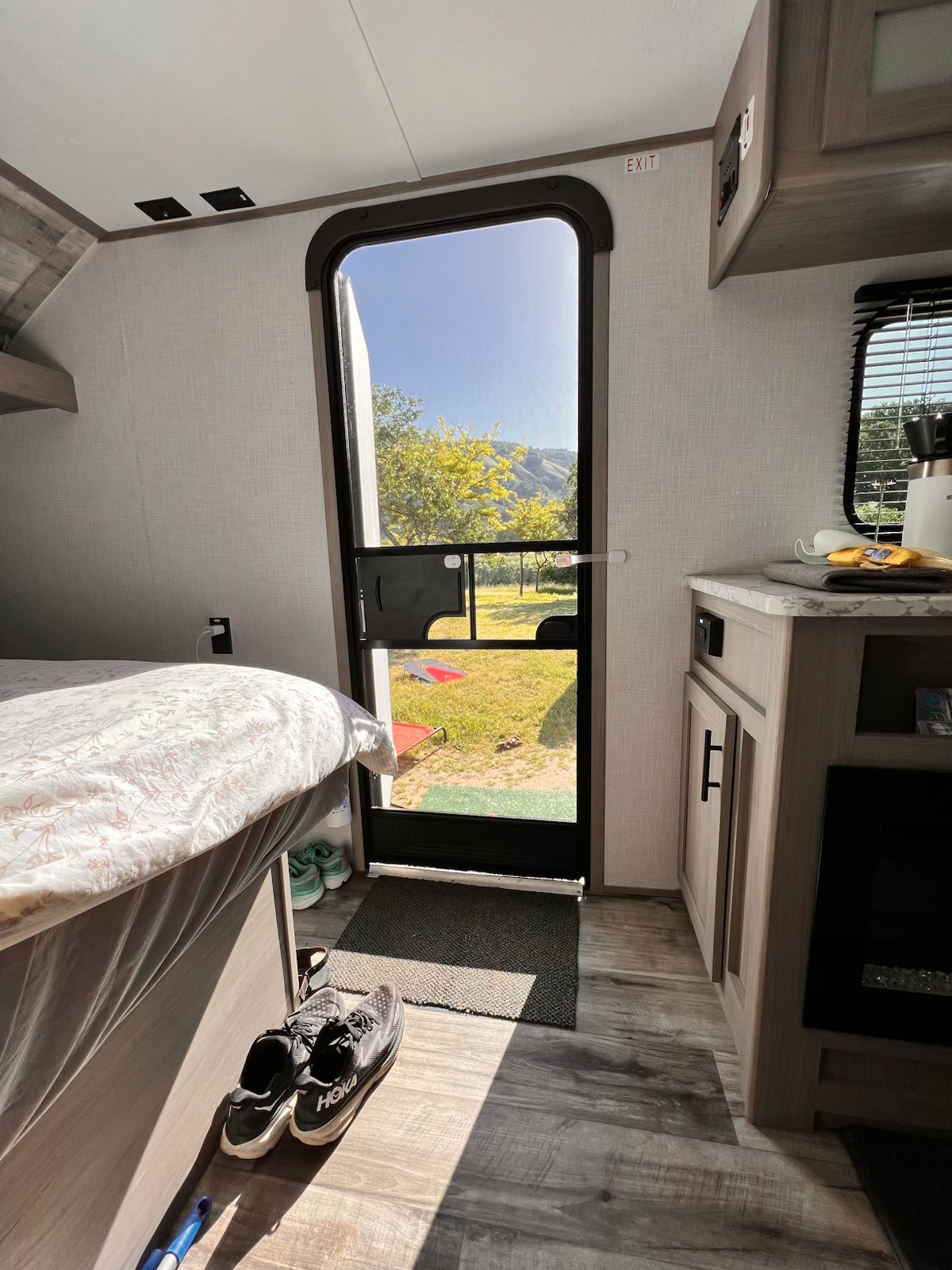 Step into this bright RV rental, featuring a cozy bed, kitchen nook, and views of a sunny, tree-lined landscape.. Dutchmen Coleman Lantern LT 2023
