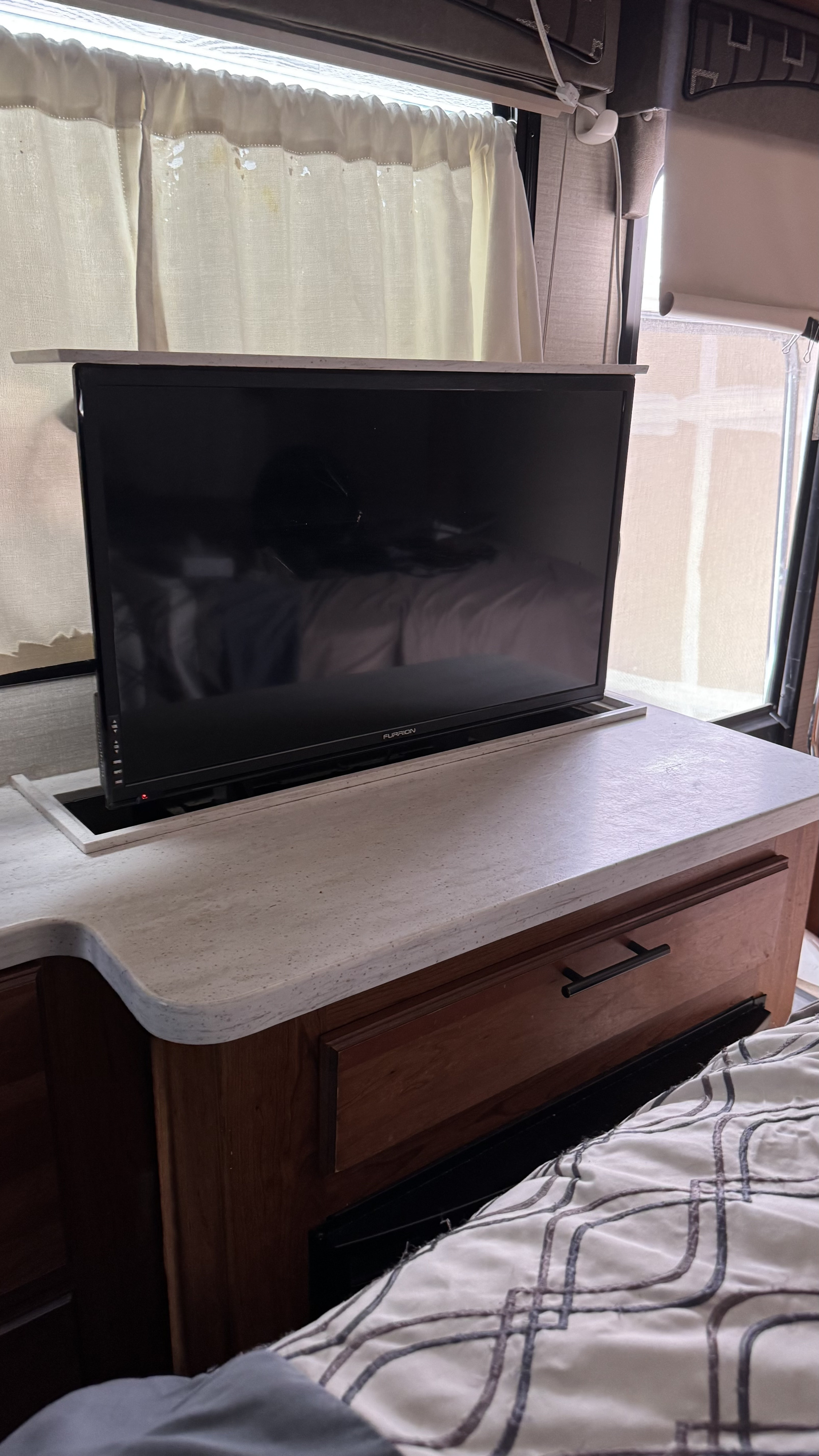 An RV rental bedroom setup featuring a pop-up TV integrated into the countertop, beside comfortable bedding and windows with curtains.. Jayco Melbourne 2017