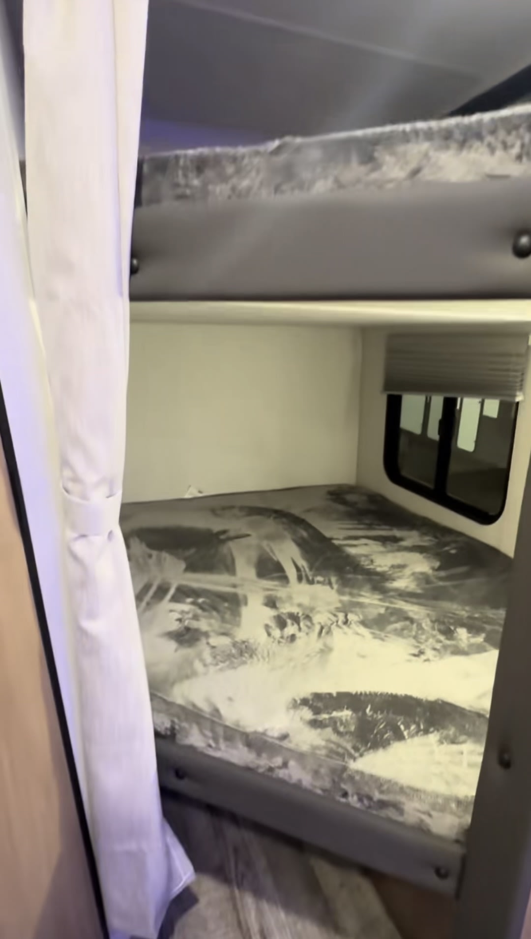 RV rental bunk beds: Two stacked beds in an RV interior with a patterned mattress, window, and white curtains on the left.. Forest River Grey Wolf 26 DBH 2024