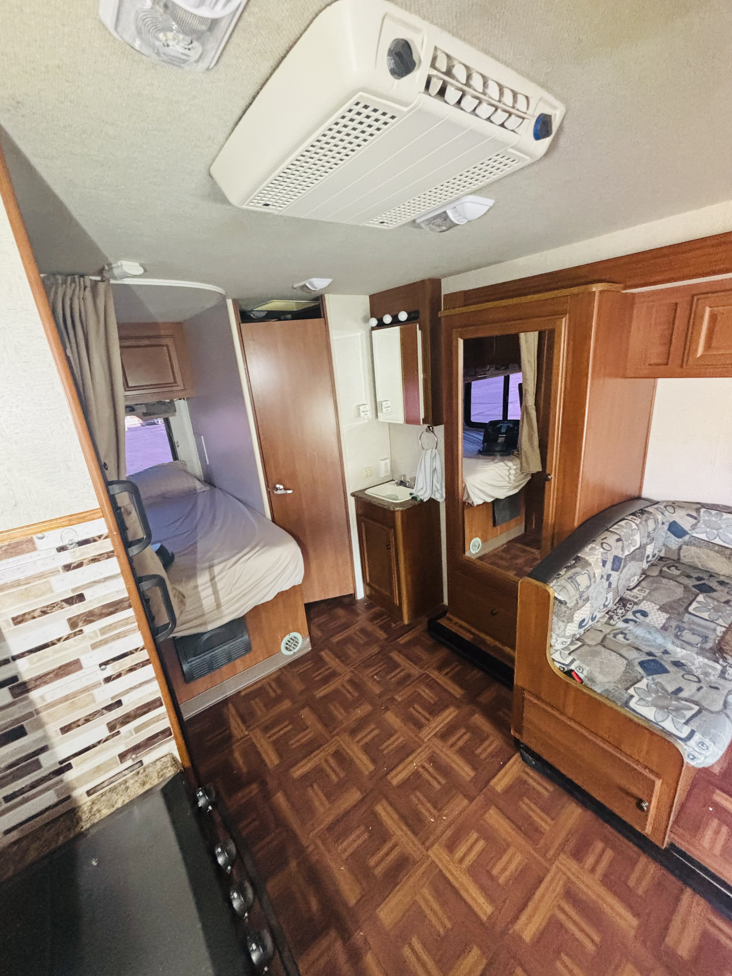 Inside an RV rental: view of the bed area, compact bathroom with sink, patterned couch, and kitchen counter. Designed for travel.. Jamboree Sport 2011