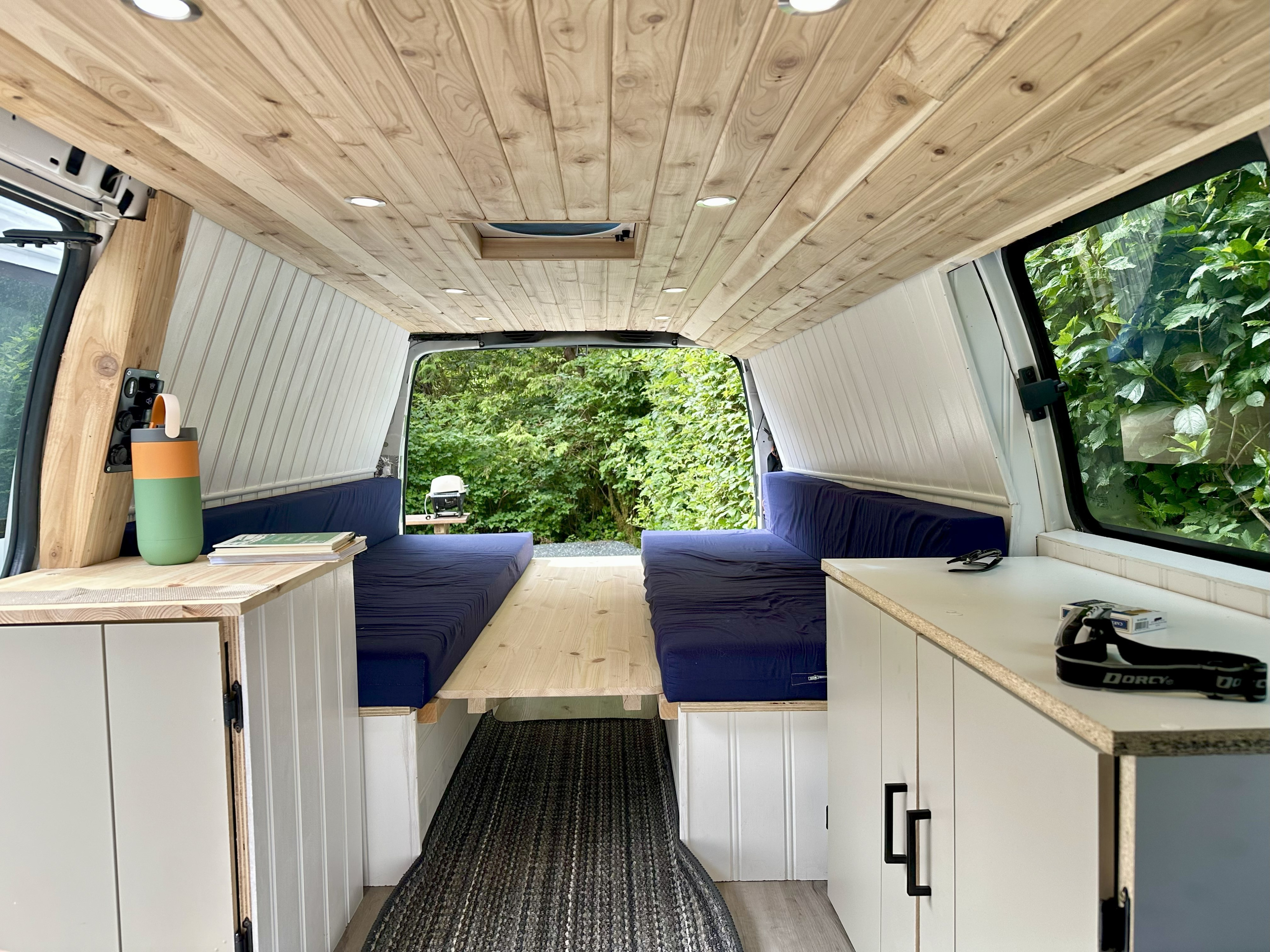 Bright RV rental camper interior with light wood ceiling, white paneled walls, and twin blue bench seating.. Gmc Savanna 2013