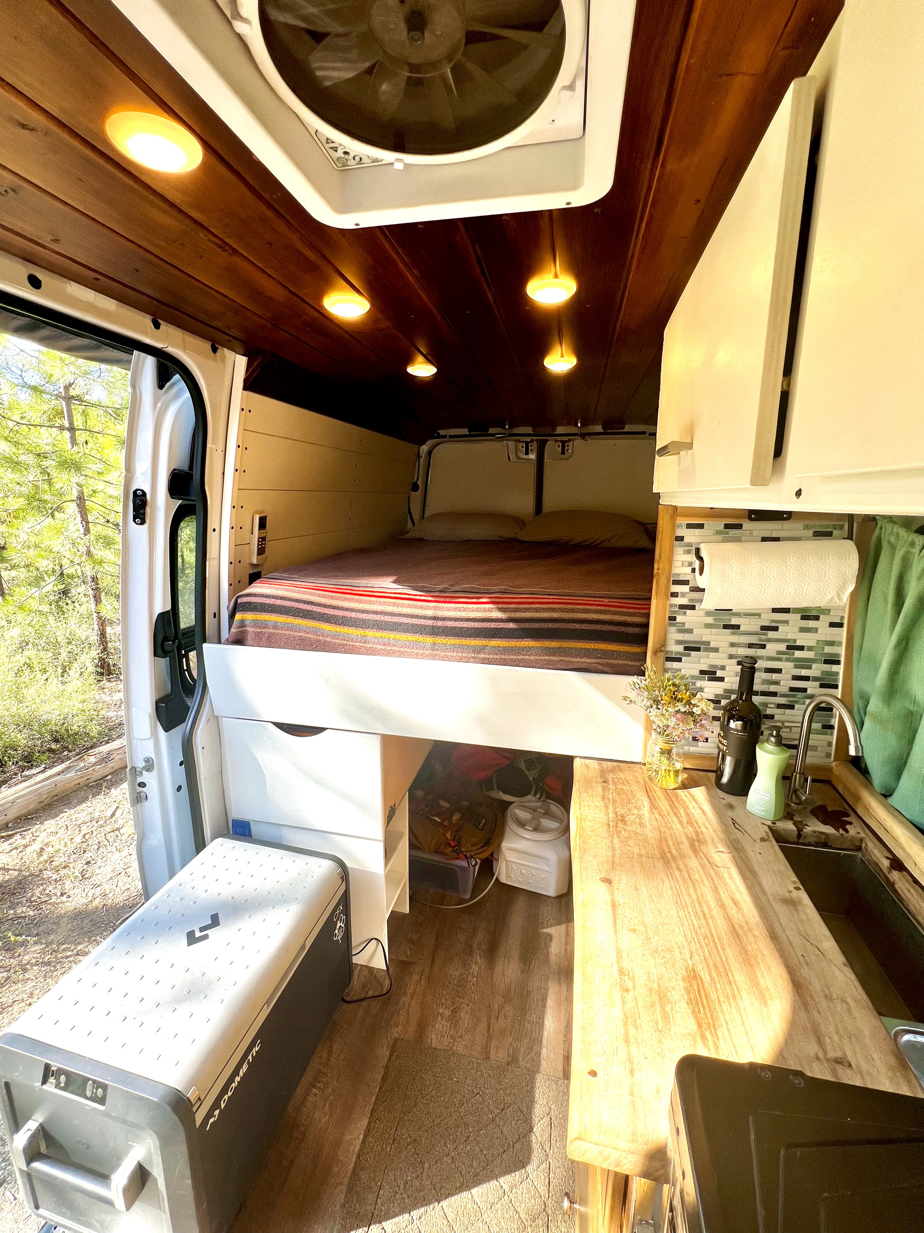 RV rental interior with a cozy bed, compact kitchen, smart storage, and natural light from the open side door.. Mercedes-Benz Sprinter 2015