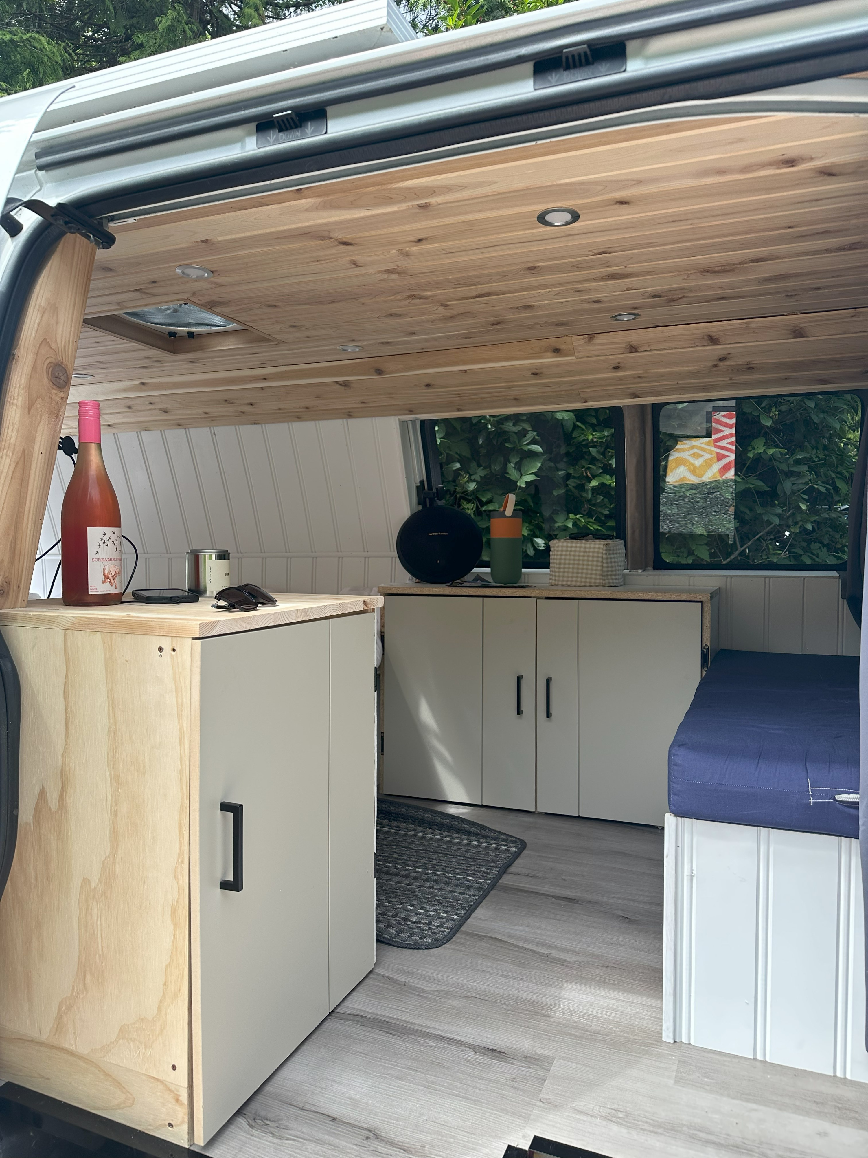 Cozy RV rental interior: wood ceiling, white walls, compact kitchen, and a comfy blue bed.. Gmc Savanna 2013