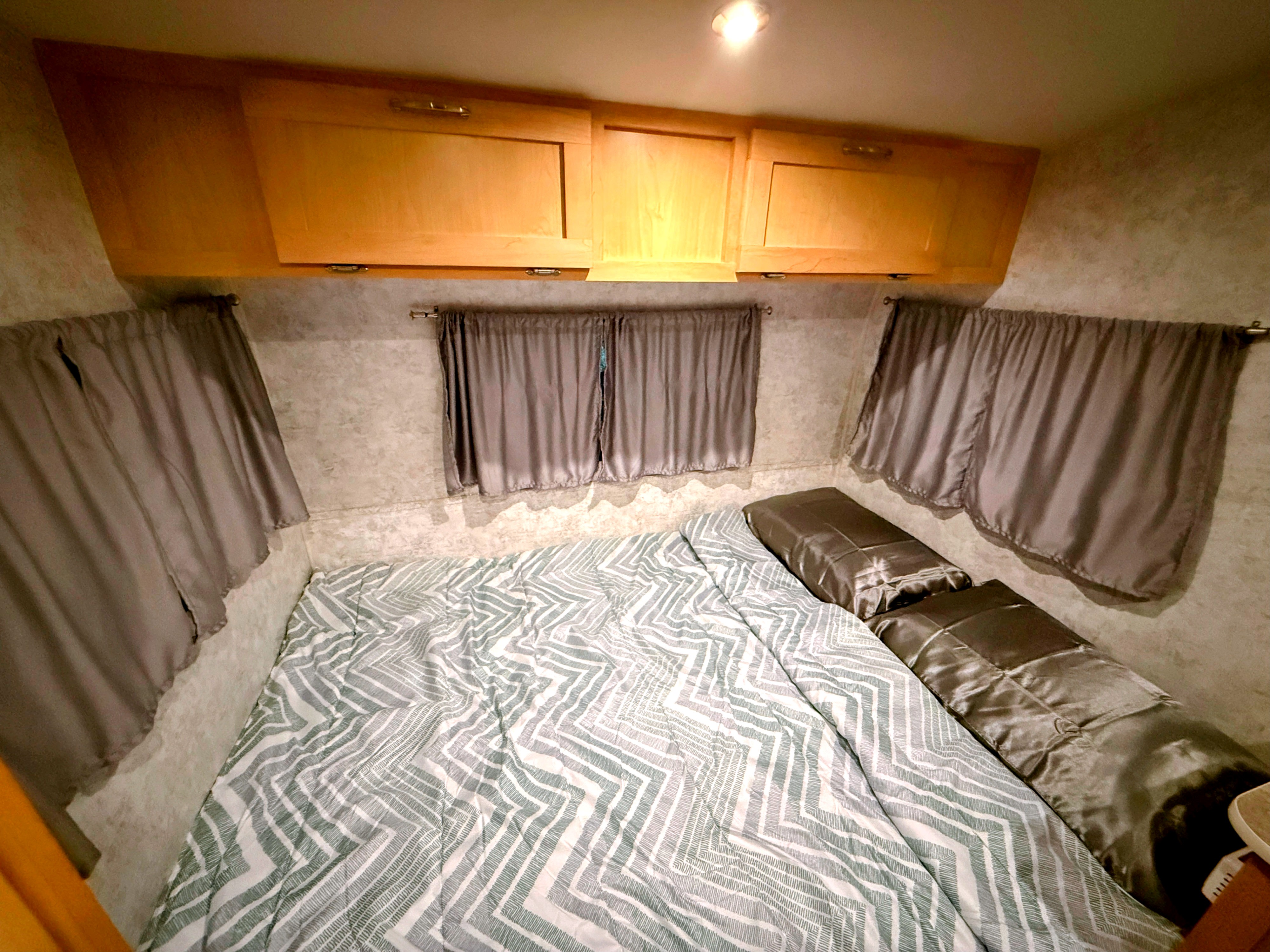 Cozy RV rental bedroom with a geometric comforter, soft pillows, and overhead wooden cabinets.. Prolite Prolite Trailer 2013