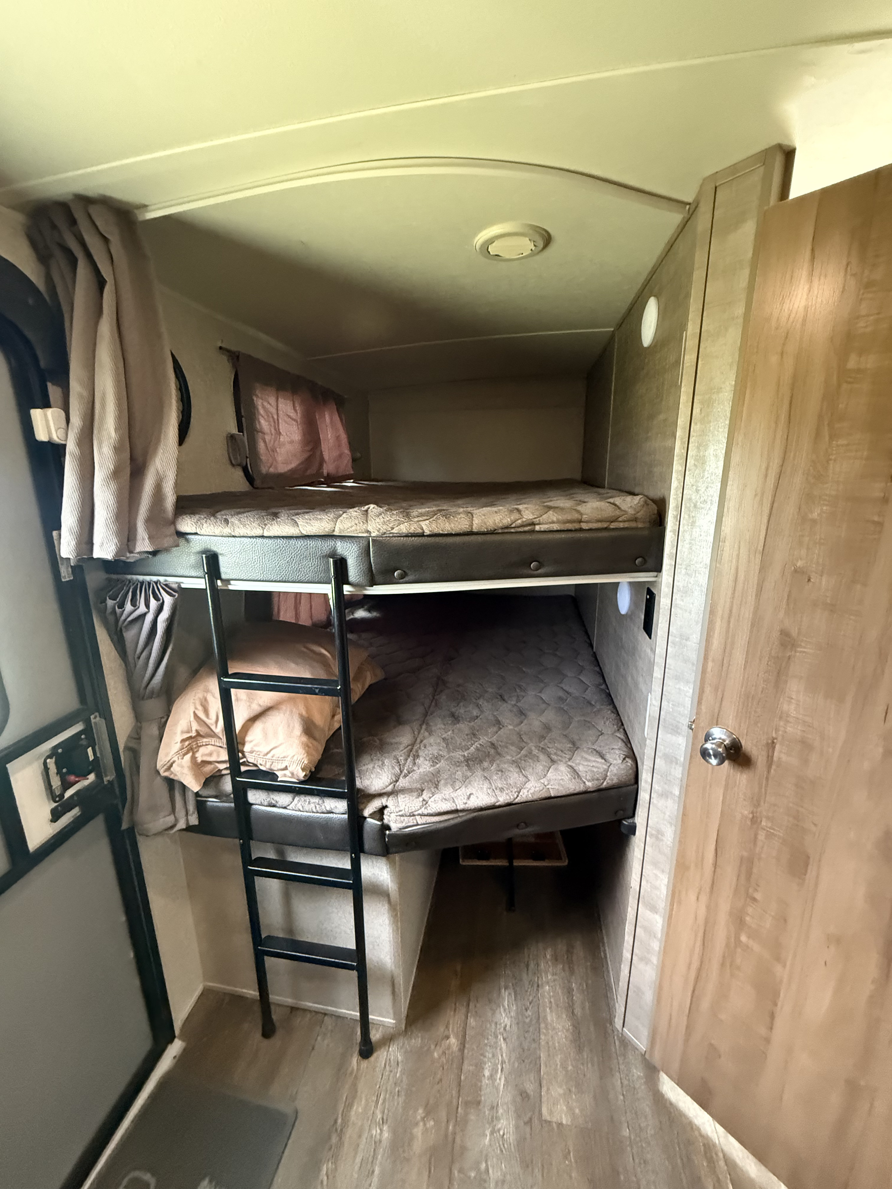 RV rental bunk room featuring two beds, a ladder, curtains, and wood-look flooring inside a camper.. Forest River Rockwood Ultra Lite 2018
