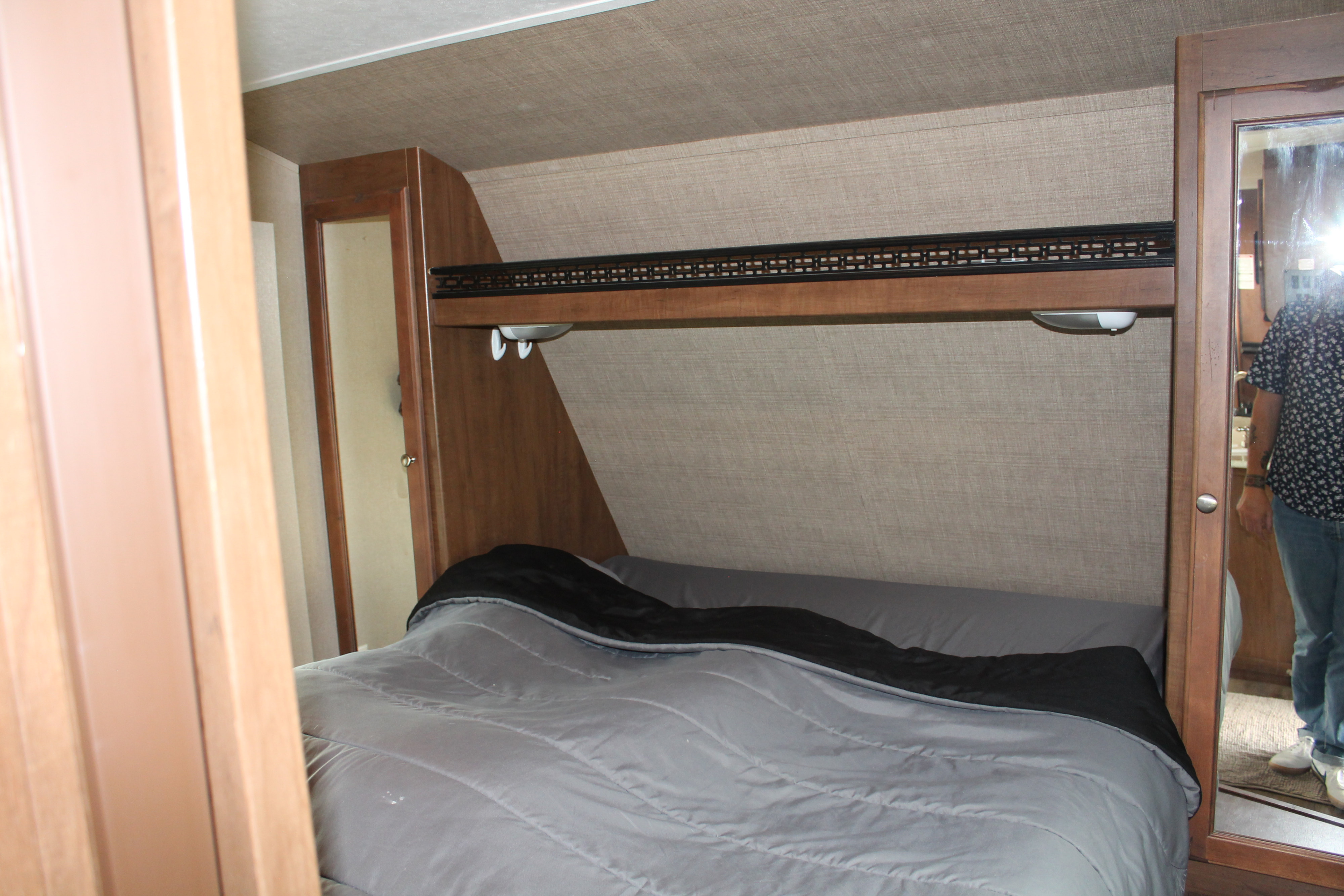 Comfortable bedroom in an RV rental, featuring a bed, overhead shelf with lights, and a full-length mirror.. Aspen Trail Aspen Trail Trailer 2015