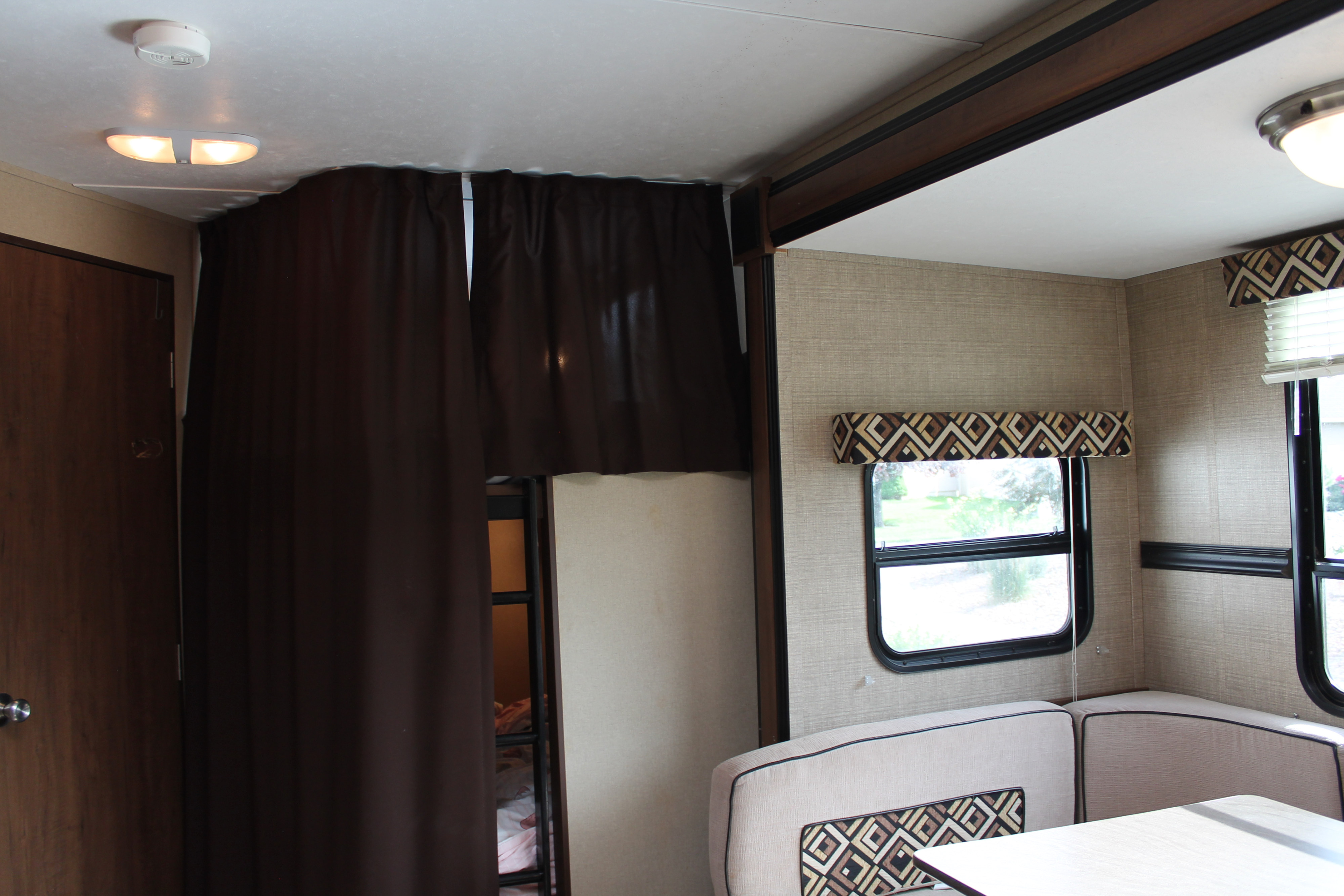 Cozy RV rental interior with dinette seating, large windows, and bunk beds behind privacy curtains.. Aspen Trail Aspen Trail Trailer 2015