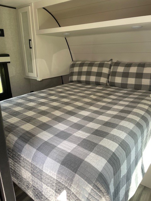 Inside a modern RV rental, a cozy bedroom with a grey and white plaid bed, sleek overhead cabinets, and reading lights.. Jayco Jay Flight SLX 2024