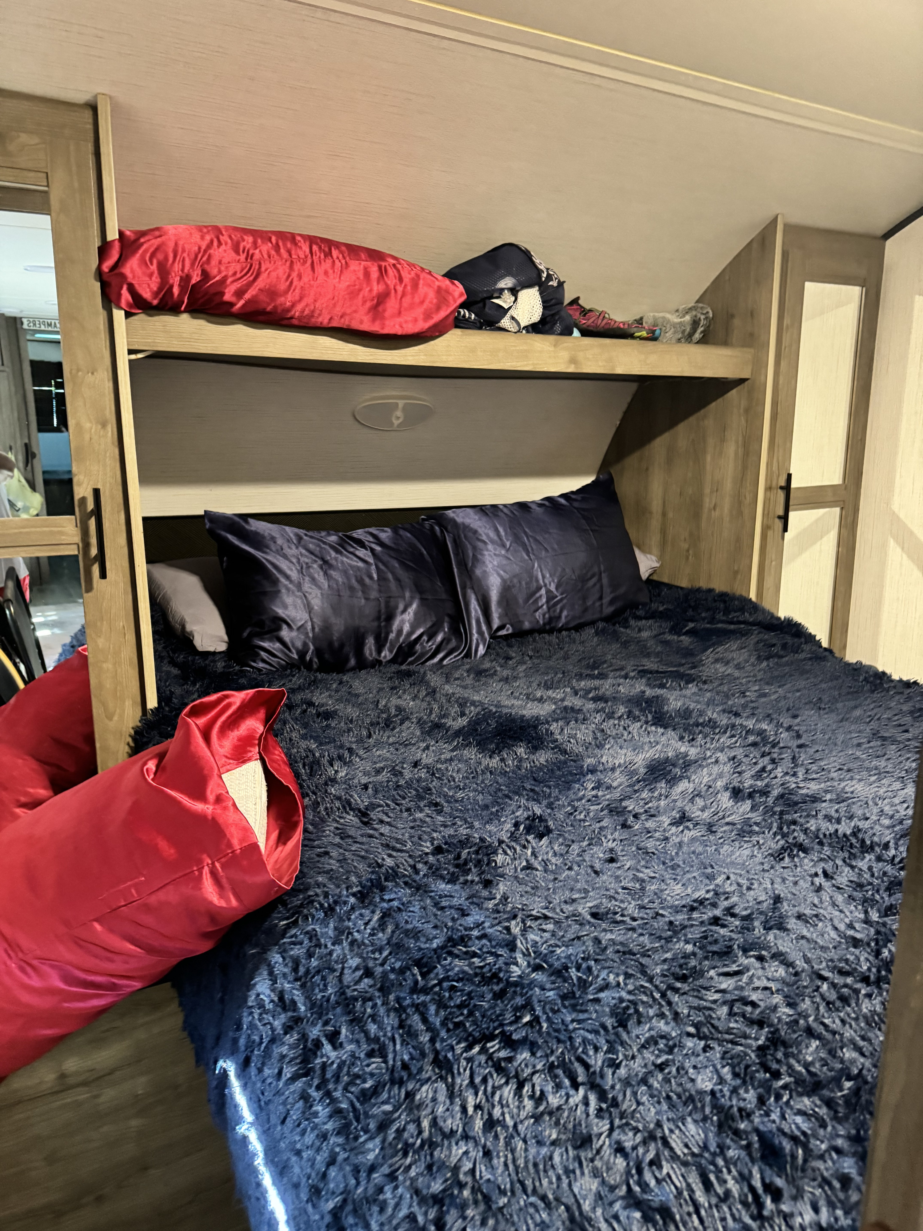 This RV rental features a cozy bunk bed setup: a dark blue fluffy lower bed with pillows, and an upper bunk with a red pillow.. Heartland RVs Pioneer 2022