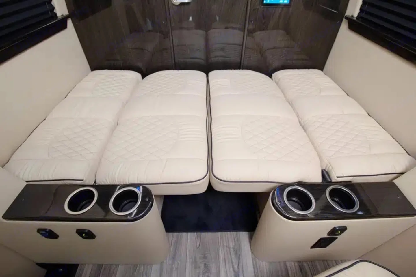 Cozy RV rental interior showing four quilted cream mattress sections folded down into a comfortable bed with cupholders.. Ultimate Toys Ultimate Cruiser 2024