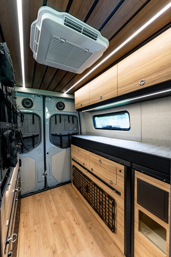 Modern RV rental interior: wood ceiling with AC, strip lighting, extensive storage, comfortable bench, and wood floor.. Mercedes Sprinter 2025