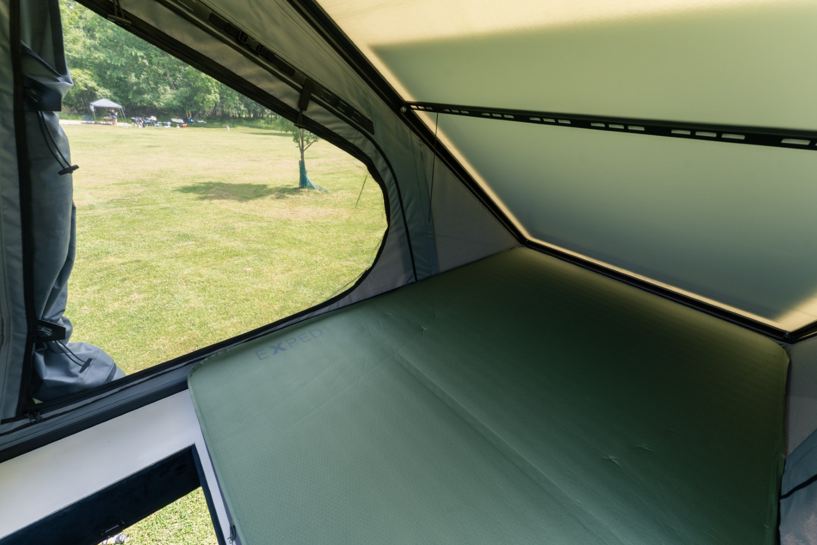 Comfortable sleeping pad inside a rooftop tent from an rv rental, with a clear view of an outdoor campsite.. Mercedes Sprinter 2025