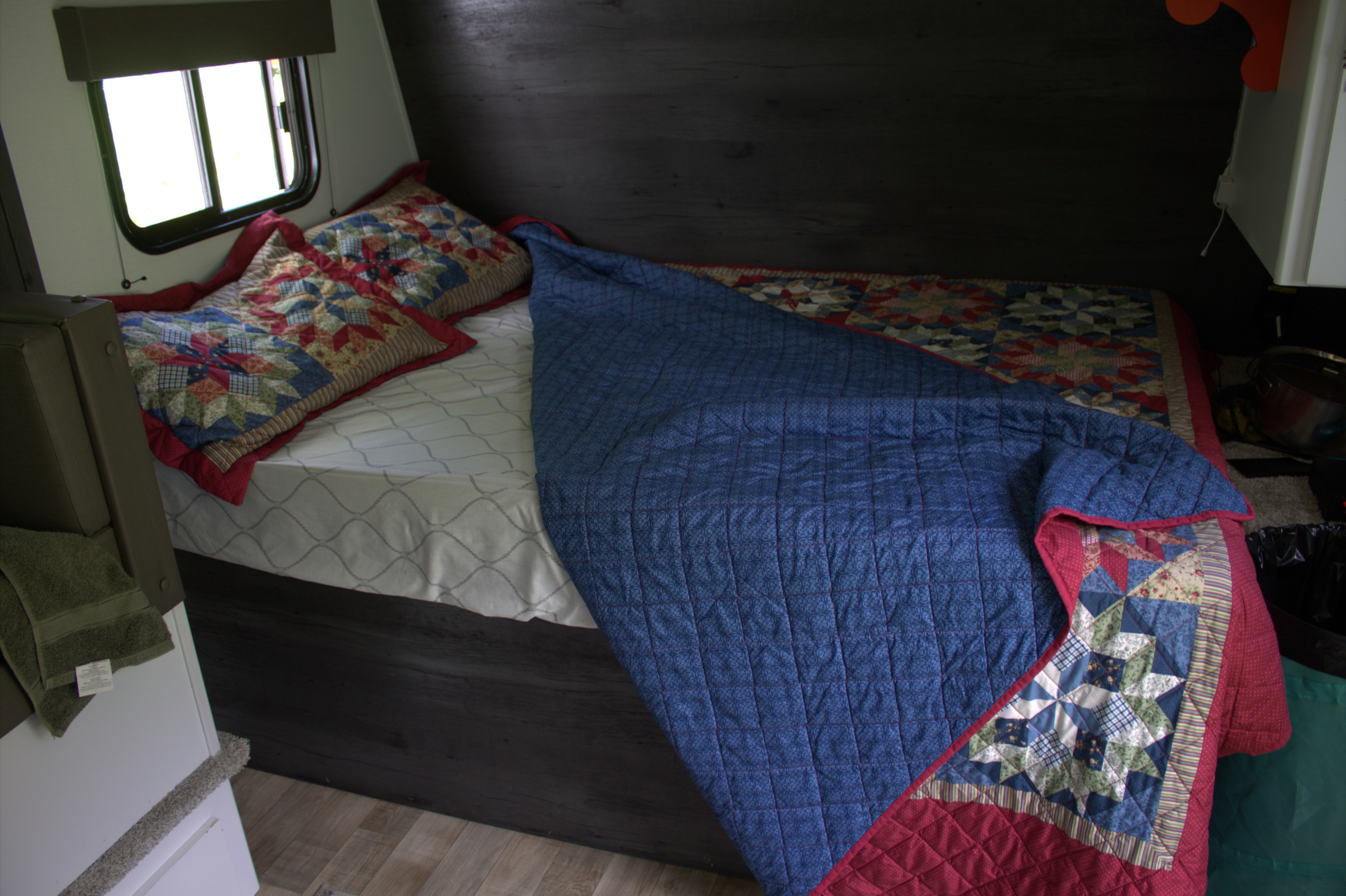 Inside an RV rental, a cozy bedroom with a bed adorned with colorful, patterned quilts and pillows, beside a window.. Keystone RV Hideout 2022
