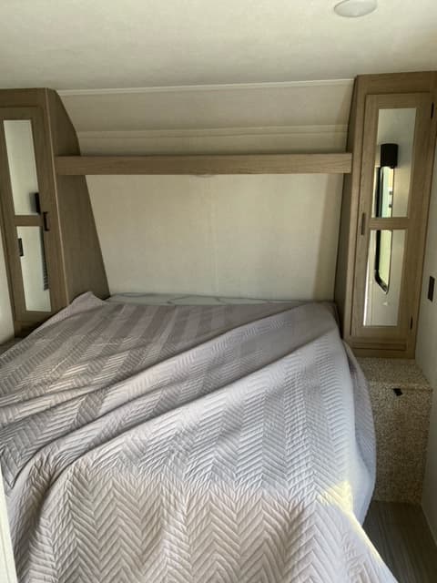 Step into comfort! This RV rental bedroom offers a quilted bed, shelving, and mirrored cabinets, ensuring a relaxing travel stay.. Keystone RV Hideout 2021