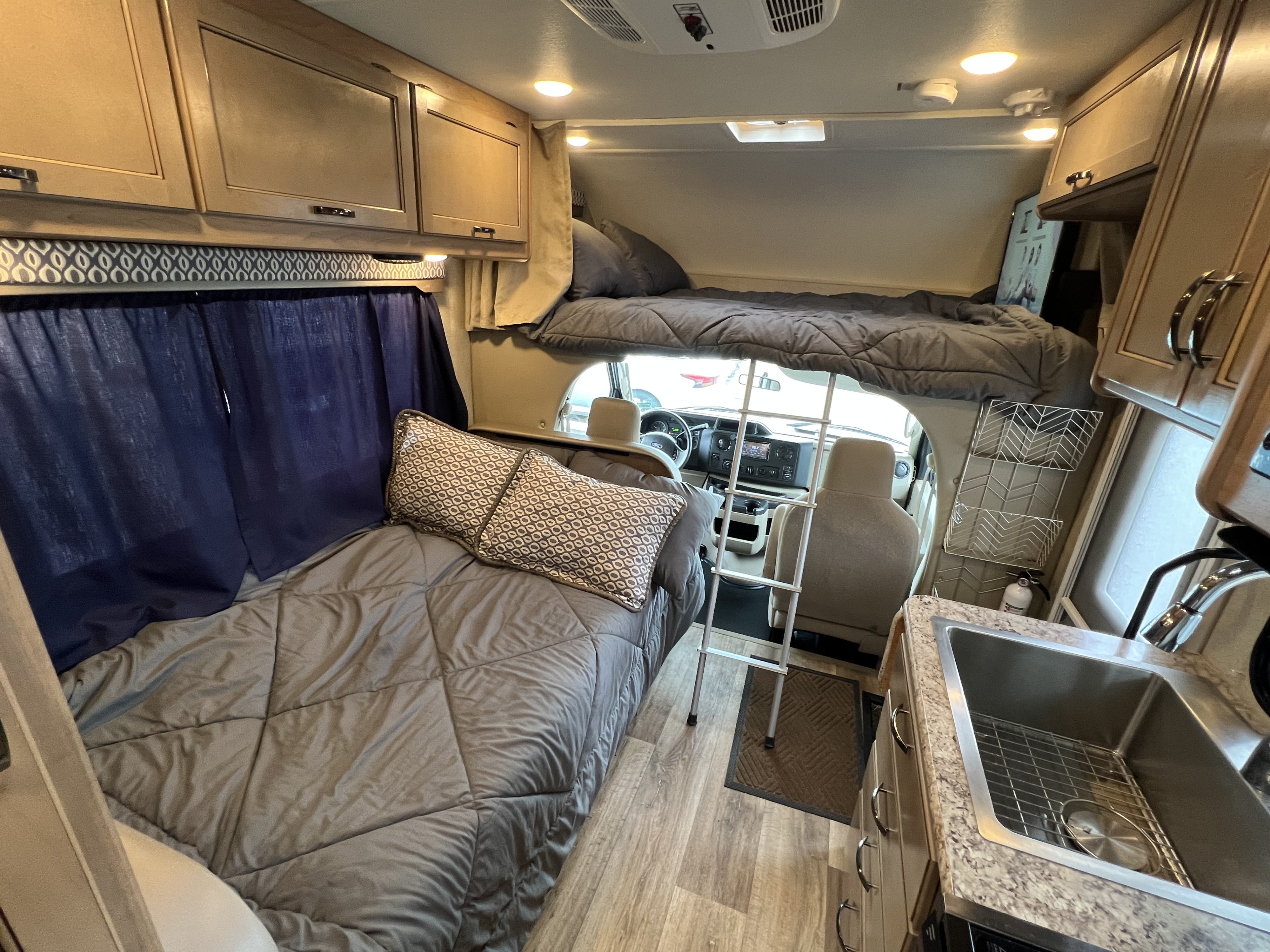 Comfortable RV rental interior: main bed with pillows, an overhead bunk with ladder, and a kitchen sink. Ready for travel.. THOR MOTOR COACH Freedom Elite 2019