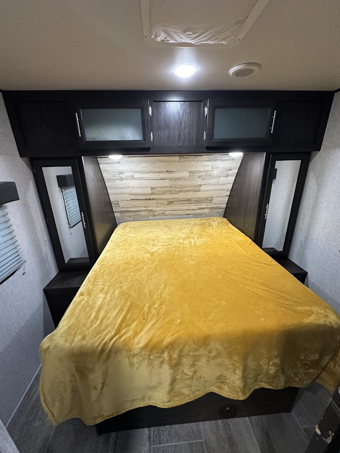 Inside an RV rental: a compact bedroom featuring a bright yellow bed, wall cabinets, and mirrors.. Dutchmen Kodiak Ultra Lite 2020
