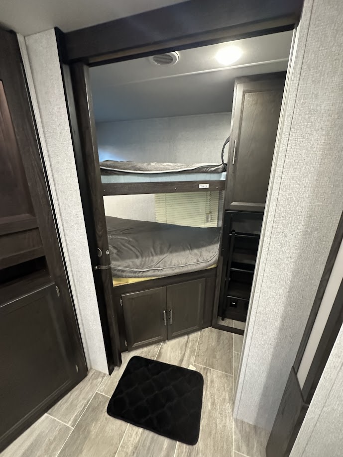 Interior of an RV rental showing stacked bunk beds, storage cabinets, and a floor mat in a compact sleeping area.. Dutchmen Kodiak Ultra Lite 2020
