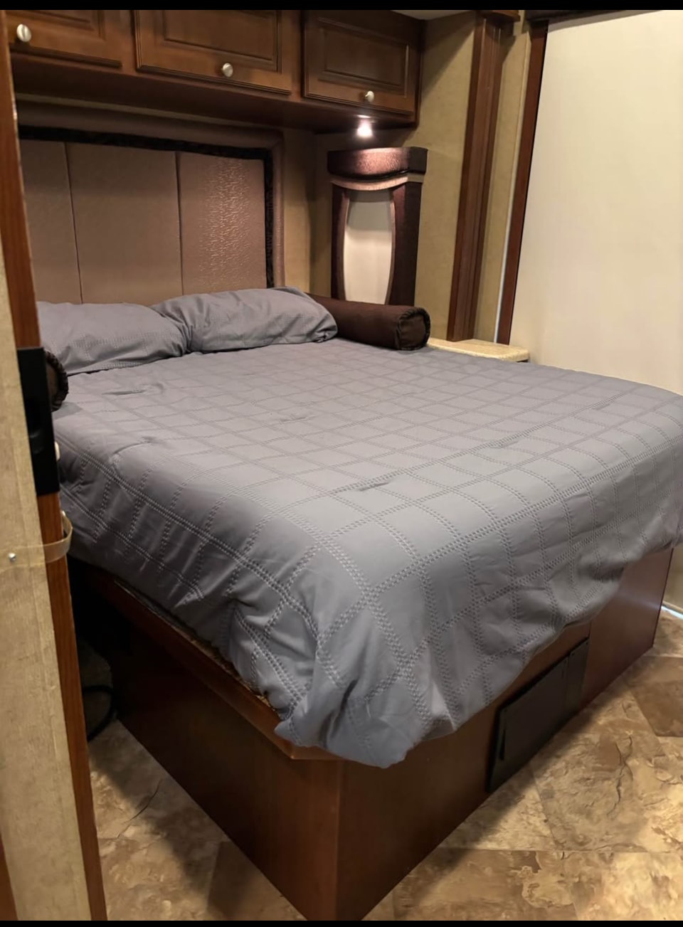 Discover comfort in this RV rental's compact bedroom. Features a neatly made bed with quilted gray bedding, pillows, and built-in storage.. Thor Outlaw 2016