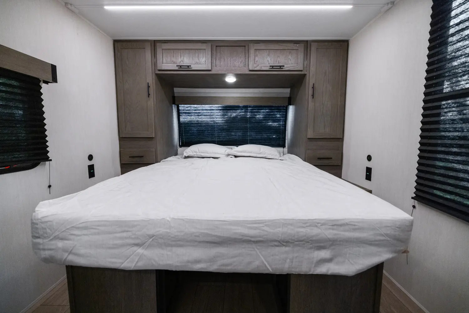Inside an RV rental, a cozy bedroom featuring a neatly made bed, built-in storage cabinets, and privacy blinds on windows.. Forest River 25RL 2025