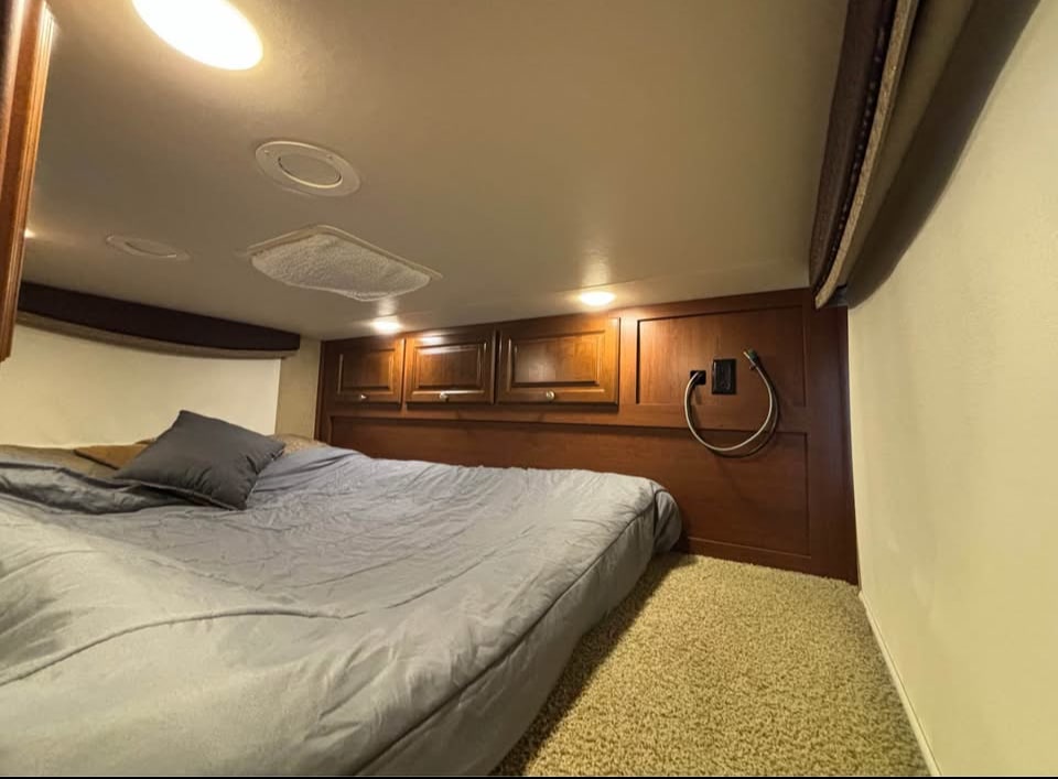 Cozy RV rental bedroom with comfortable bed, overhead cabinets, and lighting, ideal for a travel getaway.. Thor Outlaw 2016