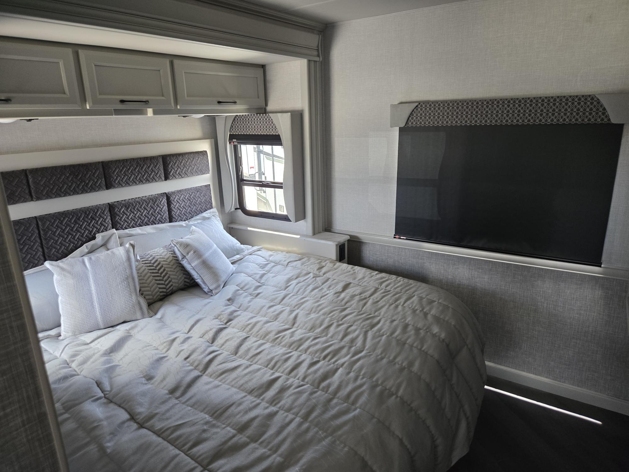 Modern RV rental bedroom interior, featuring a comfortable bed, mounted TV, and sleek overhead storage cabinets.. Fleetwood RV Bounder 33C 2025