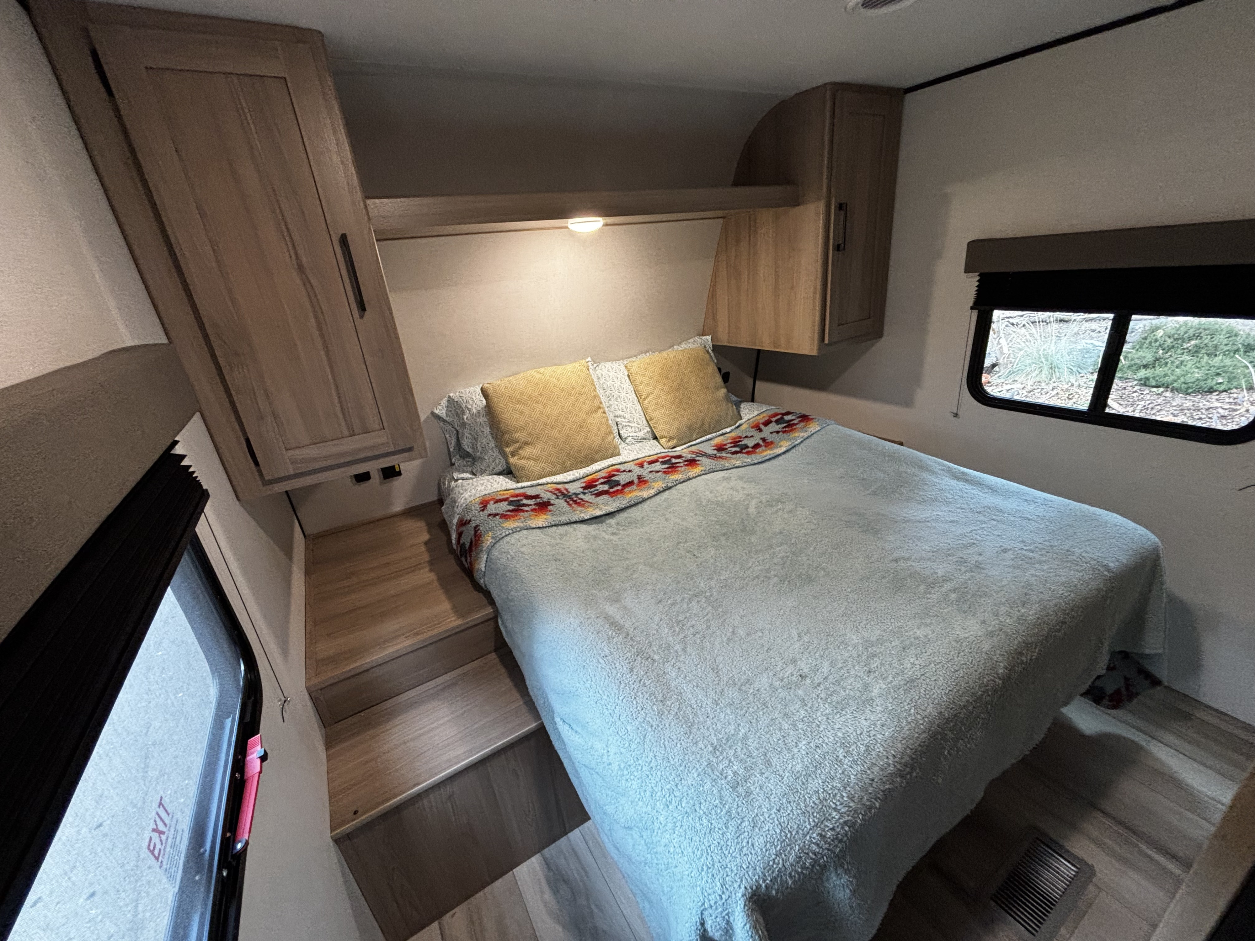 Cozy RV rental bedroom featuring a comfortable bed with steps, built-in wooden cabinetry, and a window with blinds.. Keystone Coleman Lite 22BX 2025