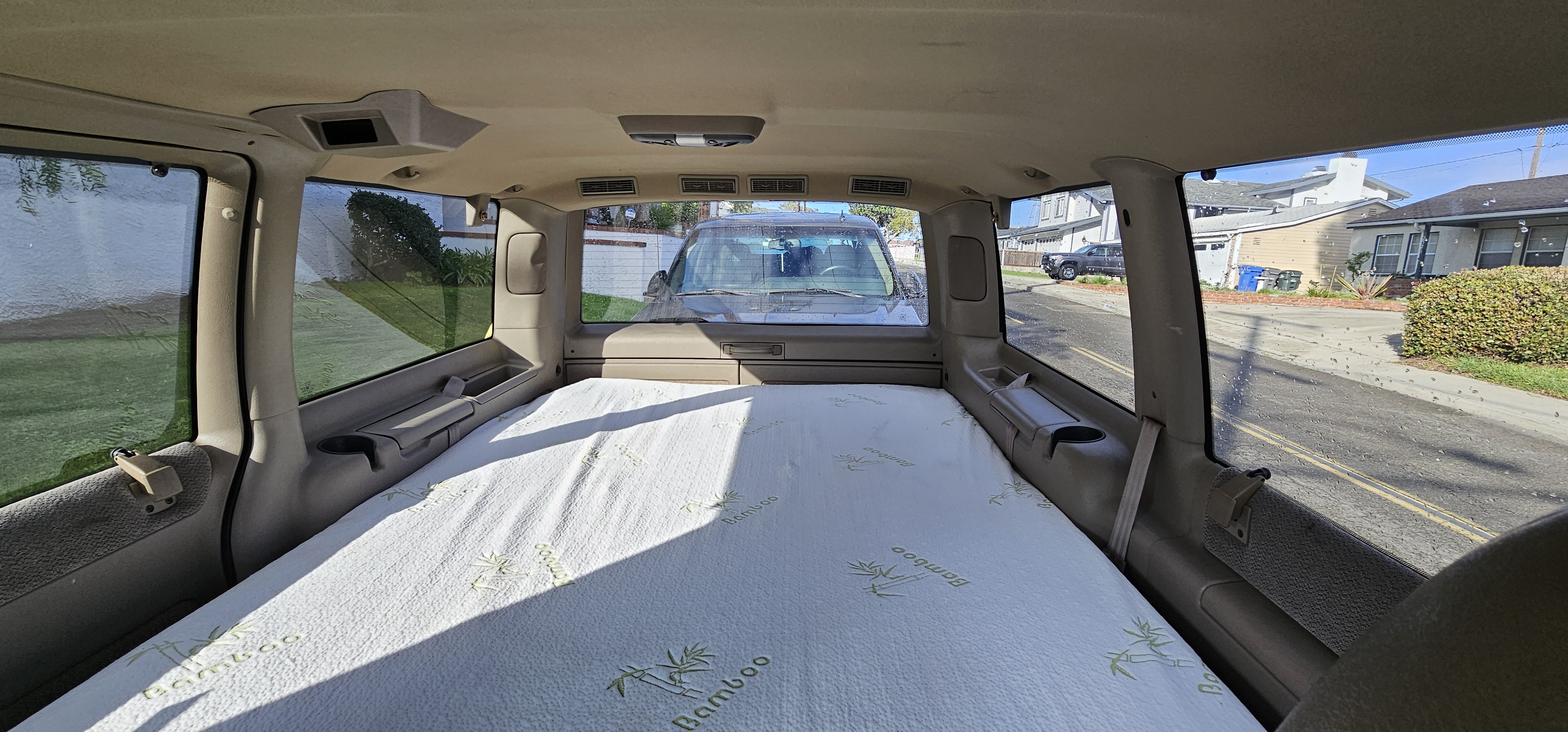 Interior of an RV rental showing a bamboo mattress set up for sleeping, with a view of a residential street outside.. Chevrolet Astro 2003