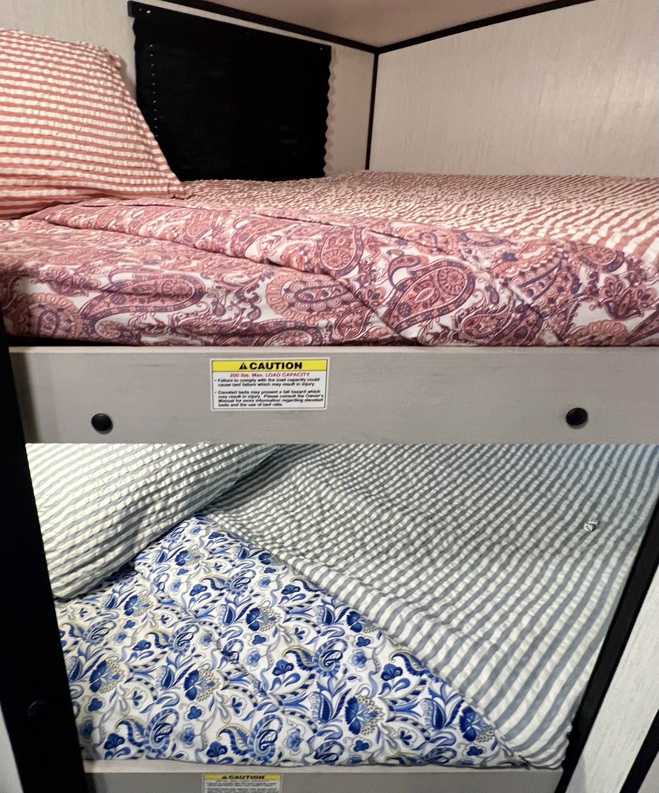 RV rental bunk beds feature colorful bedding. A safety sign warns of 200 lb. max load capacity.. Heartland RVs Mallard 2024