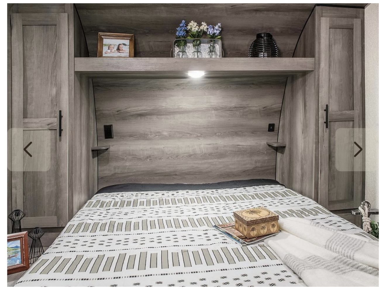 Inside a modern RV rental, a comfy bedroom features a grey woodgrain finish, patterned bedding, and practical storage.. Sportsmen SE 2021