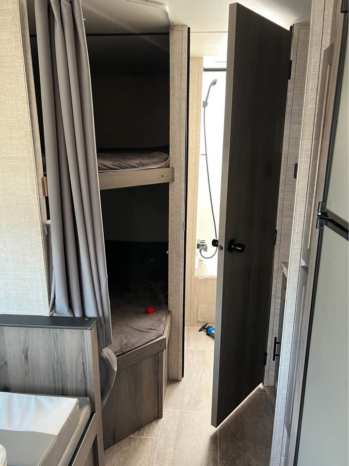 RV rental interior: bunk beds with curtain on left, compact bathroom with shower seen through open door on right.. Gulf Stream Grandriver bunkhouse 2021
