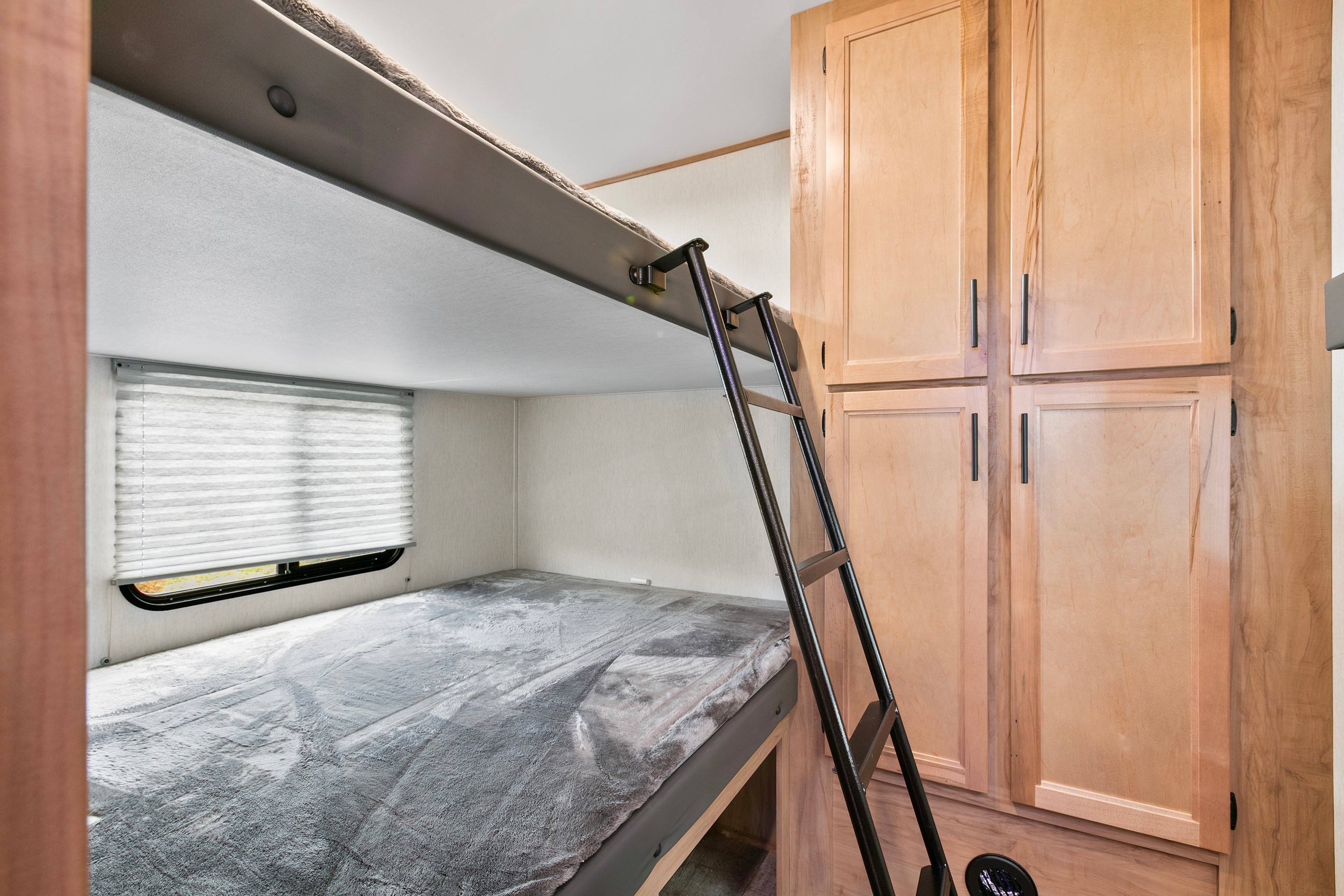 RV rental bunk beds with a ladder, window, and wooden cabinets, offering a cozy sleeping area for travelers.. Cherokee limited Arctic Wolf 2023