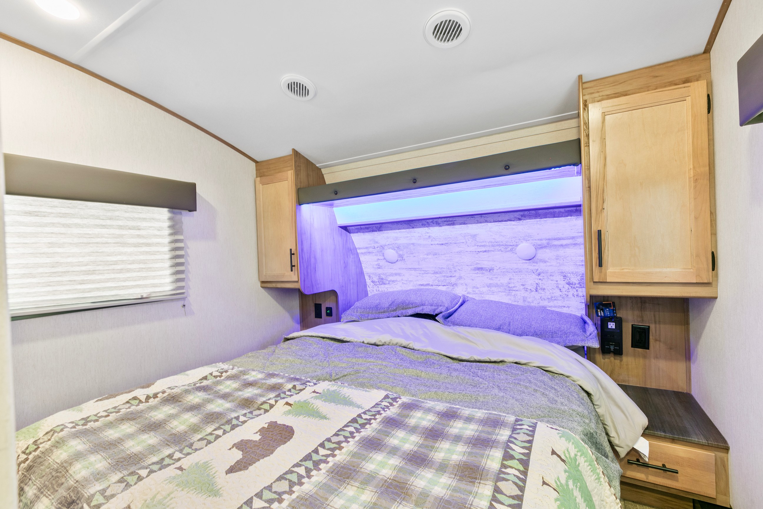 This comfortable RV rental bedroom features a cozy bed with decorative bedding, ambient purple lighting, and convenient storage.. Cherokee limited Arctic Wolf 2023