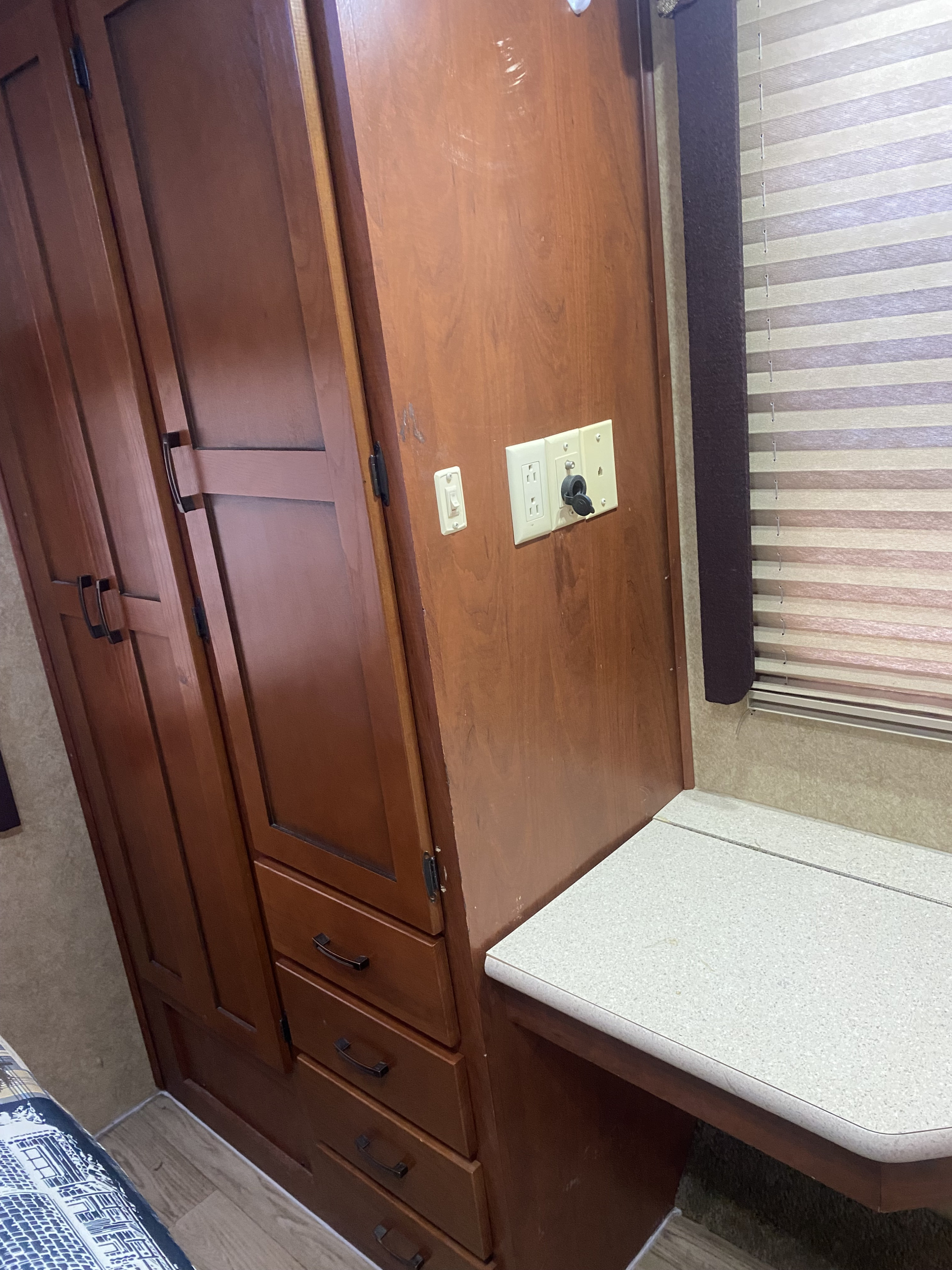 RV rental interior with warm wood cabinetry, drawers, a small desk, and striped window blinds. Electrical outlets are visible.. Forest River Sunseeker 2011
