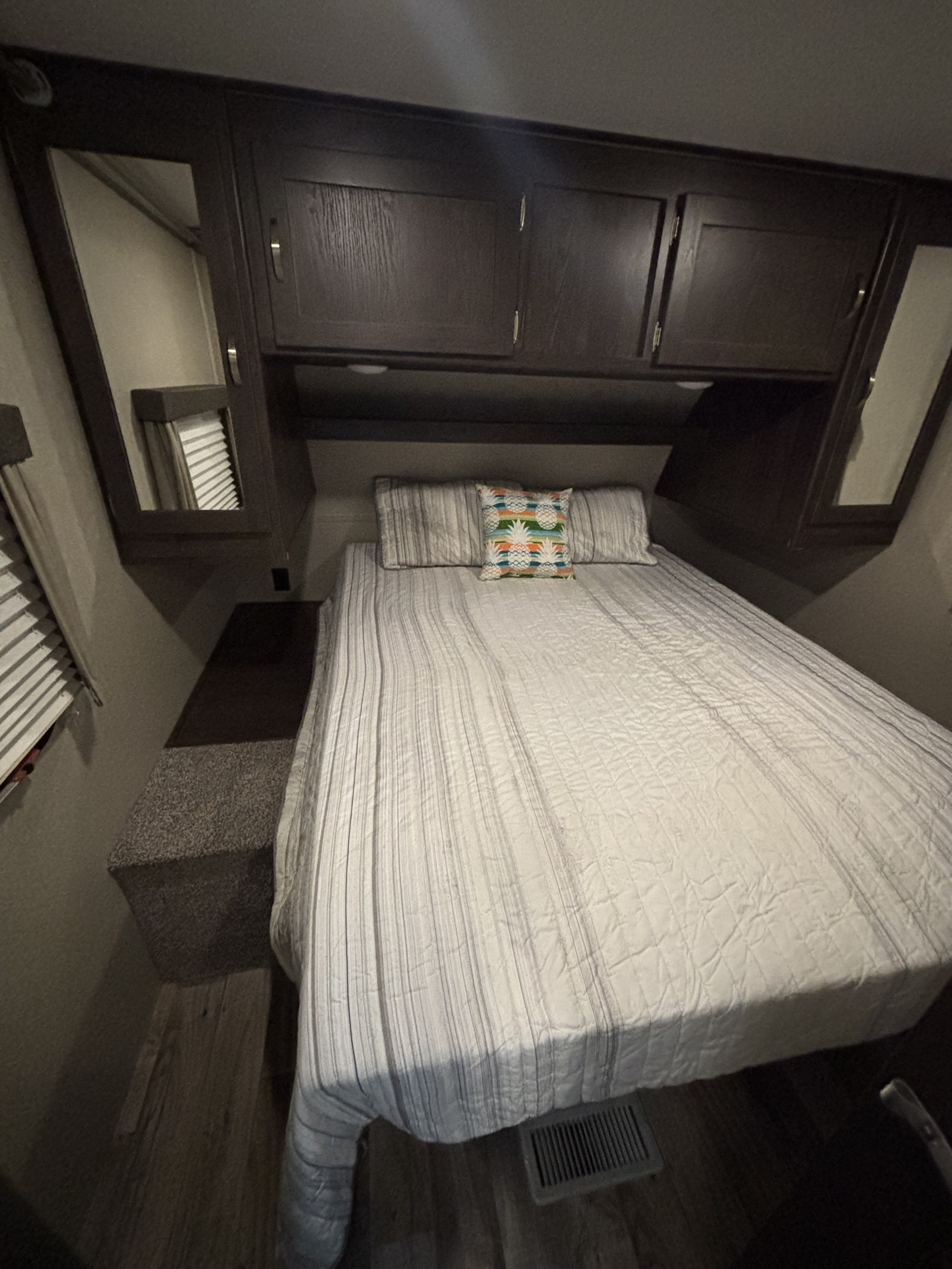 RV rental bedroom: Dark wood cabinets, striped bedding, and a decorative pillow for a cozy stay on the road.. Keystone RV Outback Ultra-Lite 2018