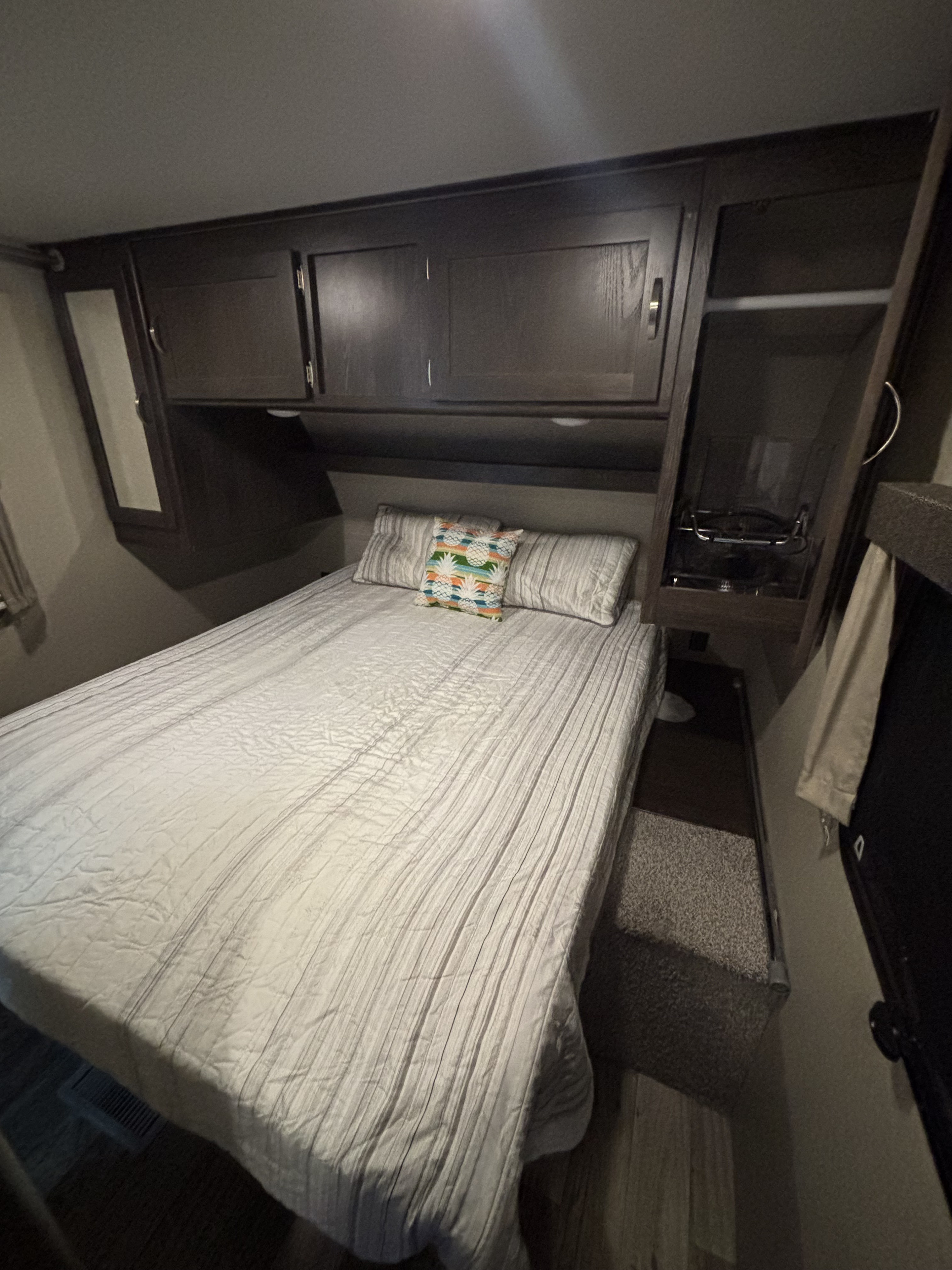 Cozy RV rental bedroom featuring a large bed with a vibrant pineapple pillow, dark wood cabinets, and a TV.. Keystone RV Outback Ultra-Lite 2018