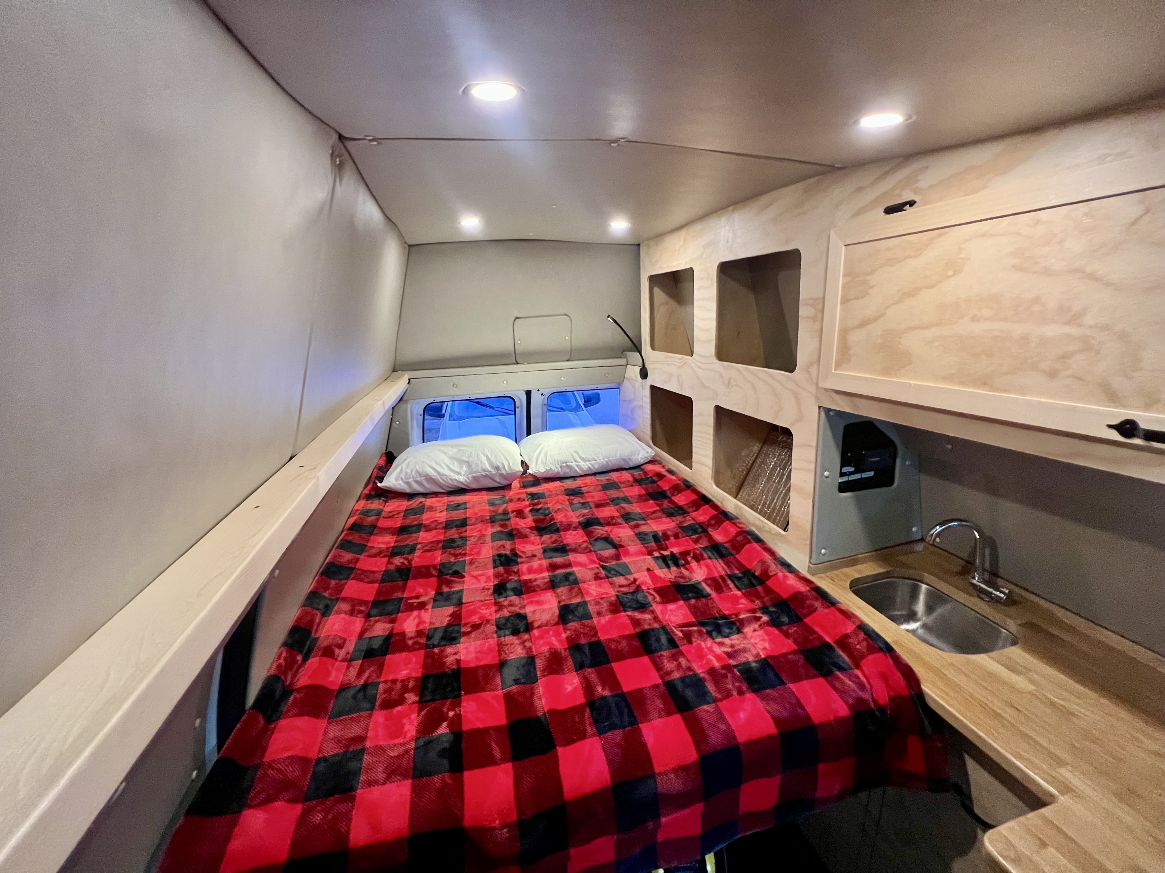 Inside this RV rental: a cozy bed with red plaid blanket, compact sink, and clever storage for your adventure.. Ford E250 Eagle Camper 2012